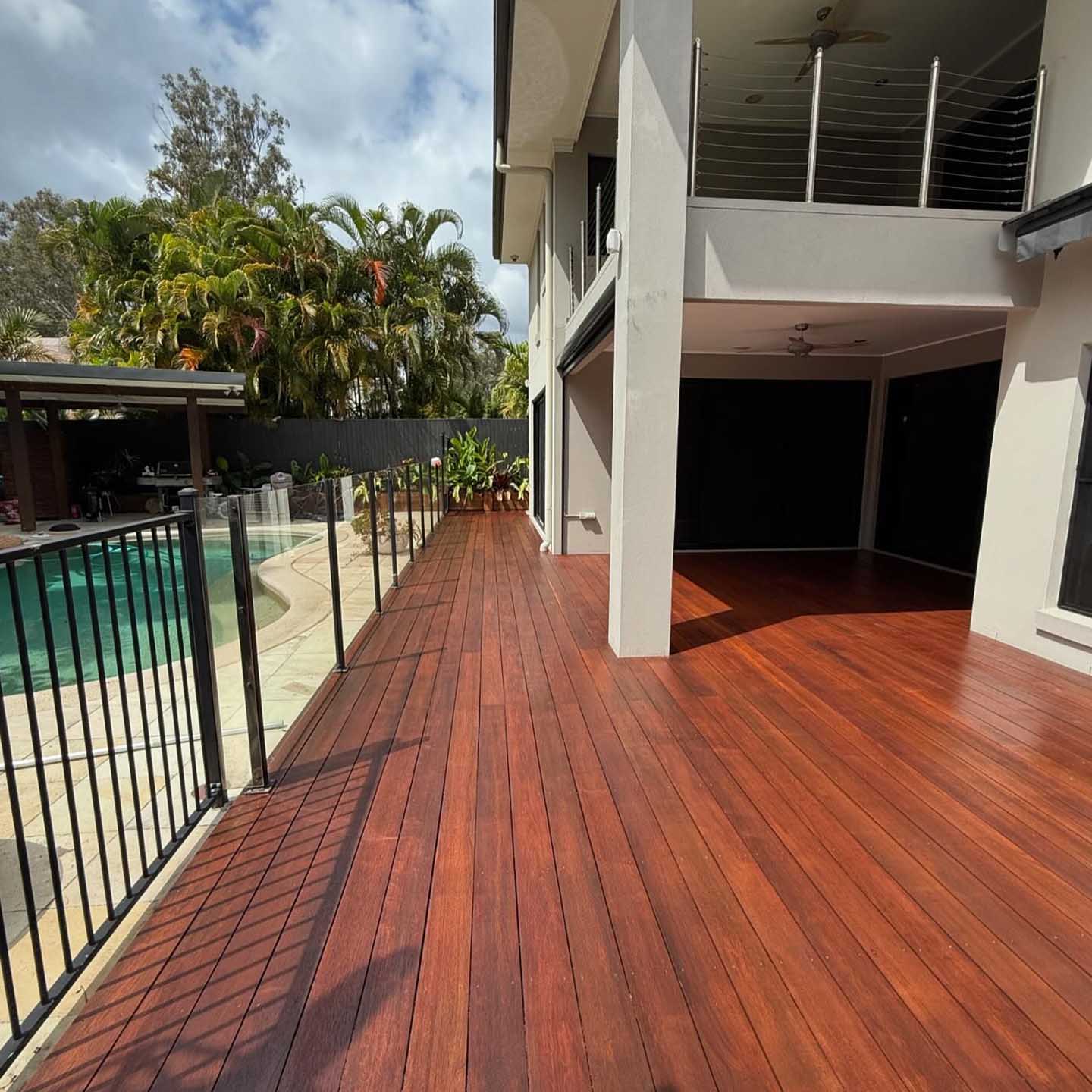 Freshly oiled timber deck along a black pool fence beside a two-storey house