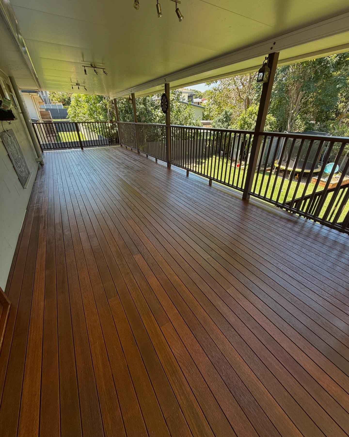 Long covered timber verandah with dark metal balustrade overlooking a backyard