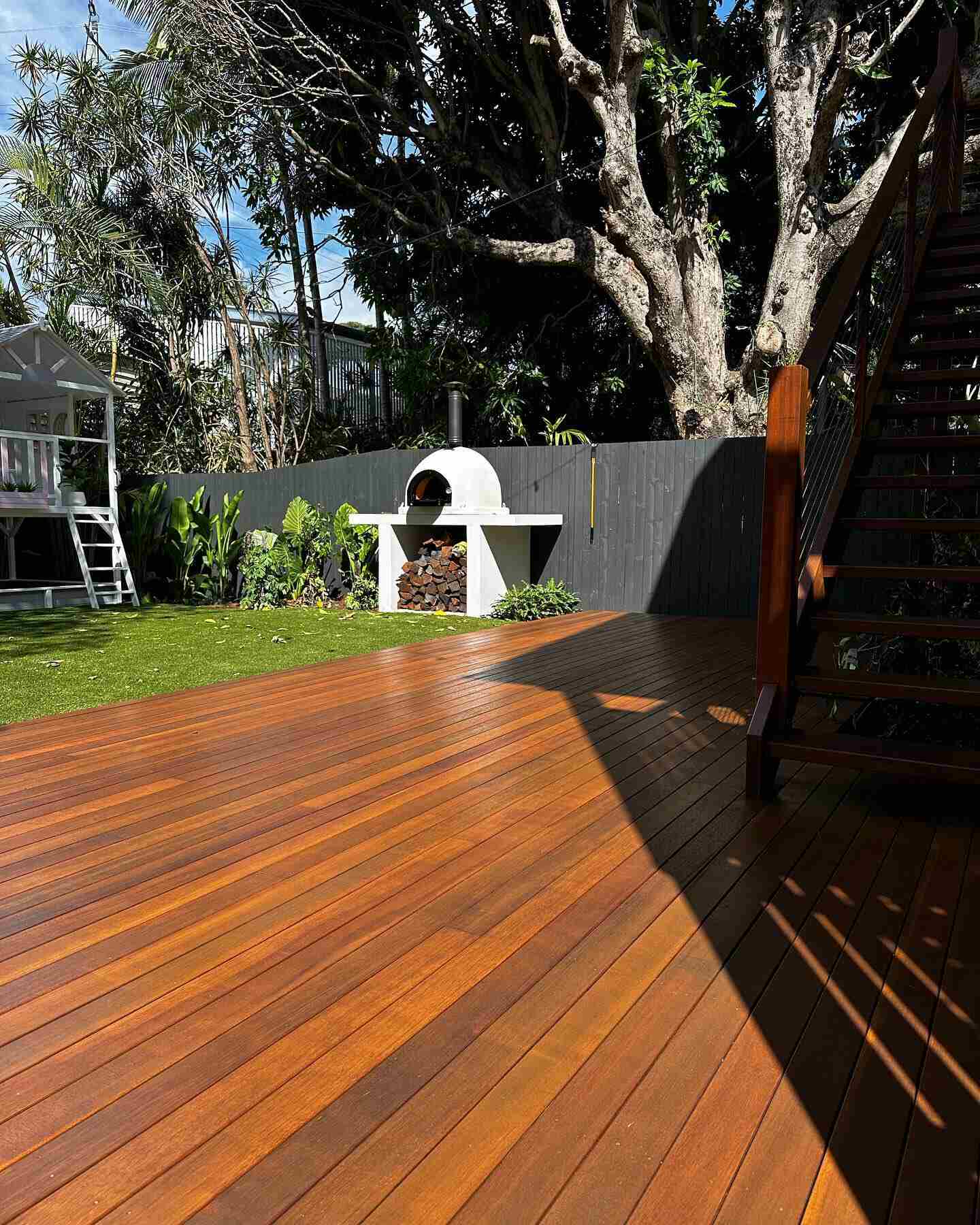 Oiled timber deck beside timber stairs, with a pizza oven and cubby house behind