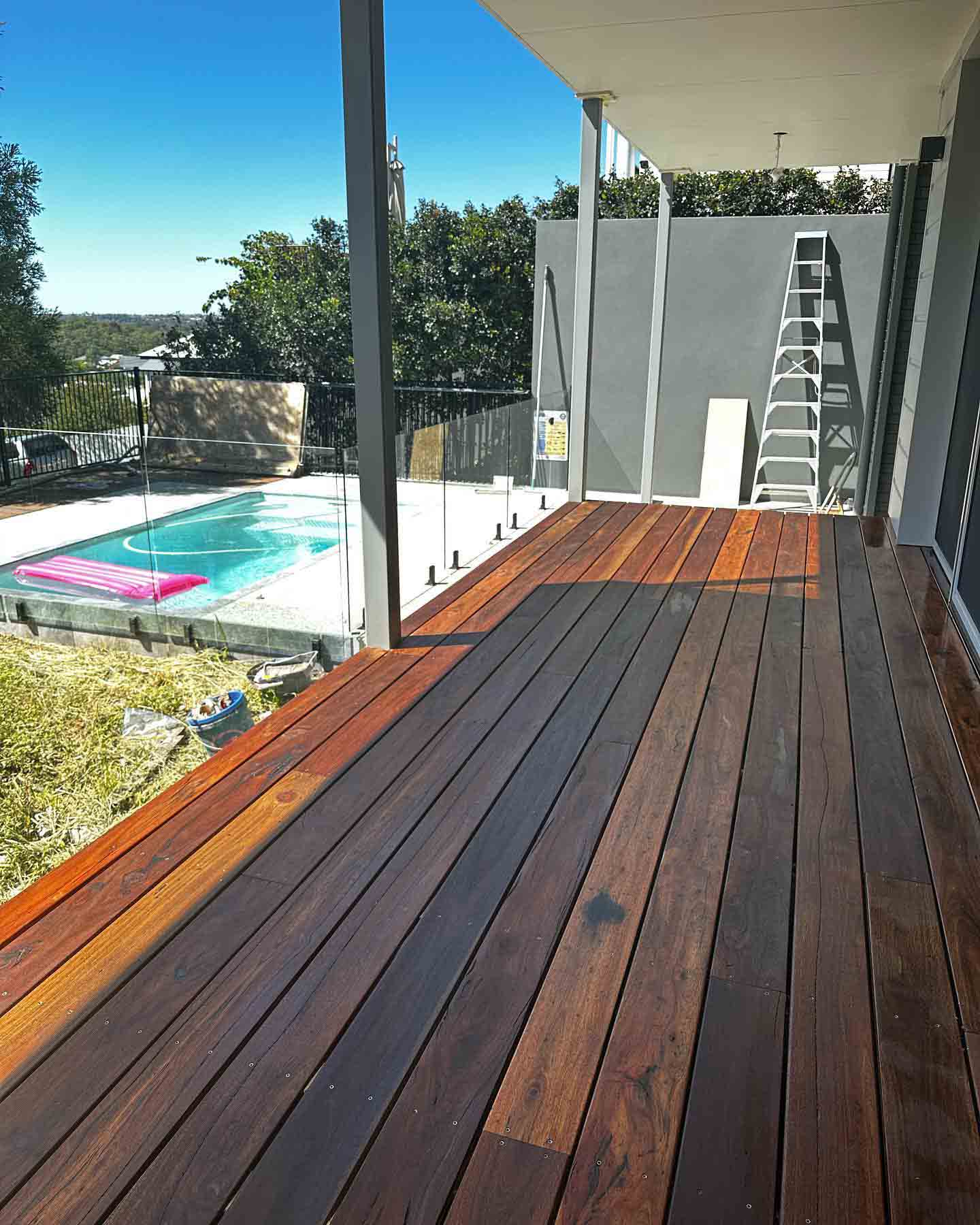 Oiled timber deck under a raised roof overlooking a glass-fenced pool