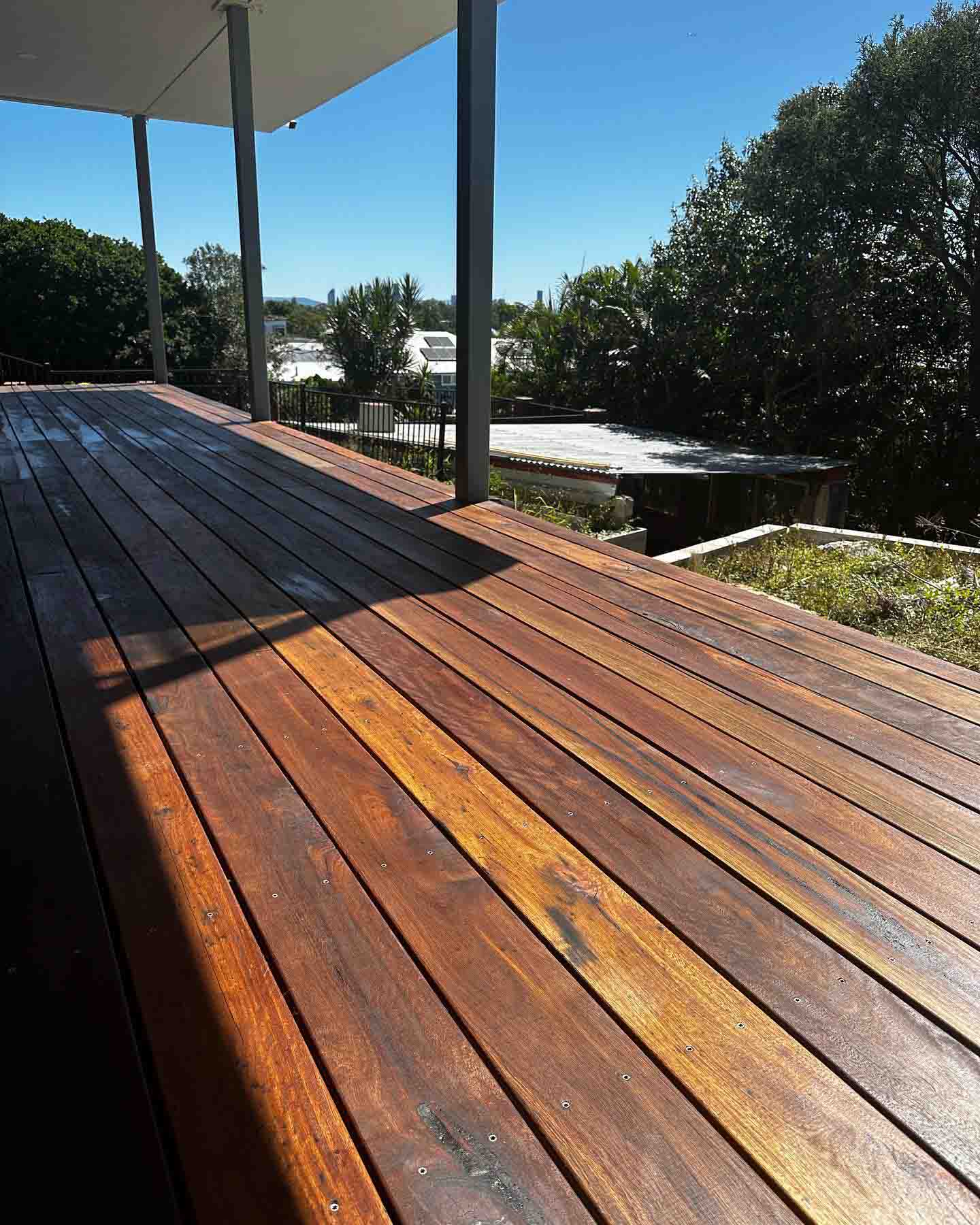 Oiled timber deck in afternoon sun with dark roof posts and treetops
