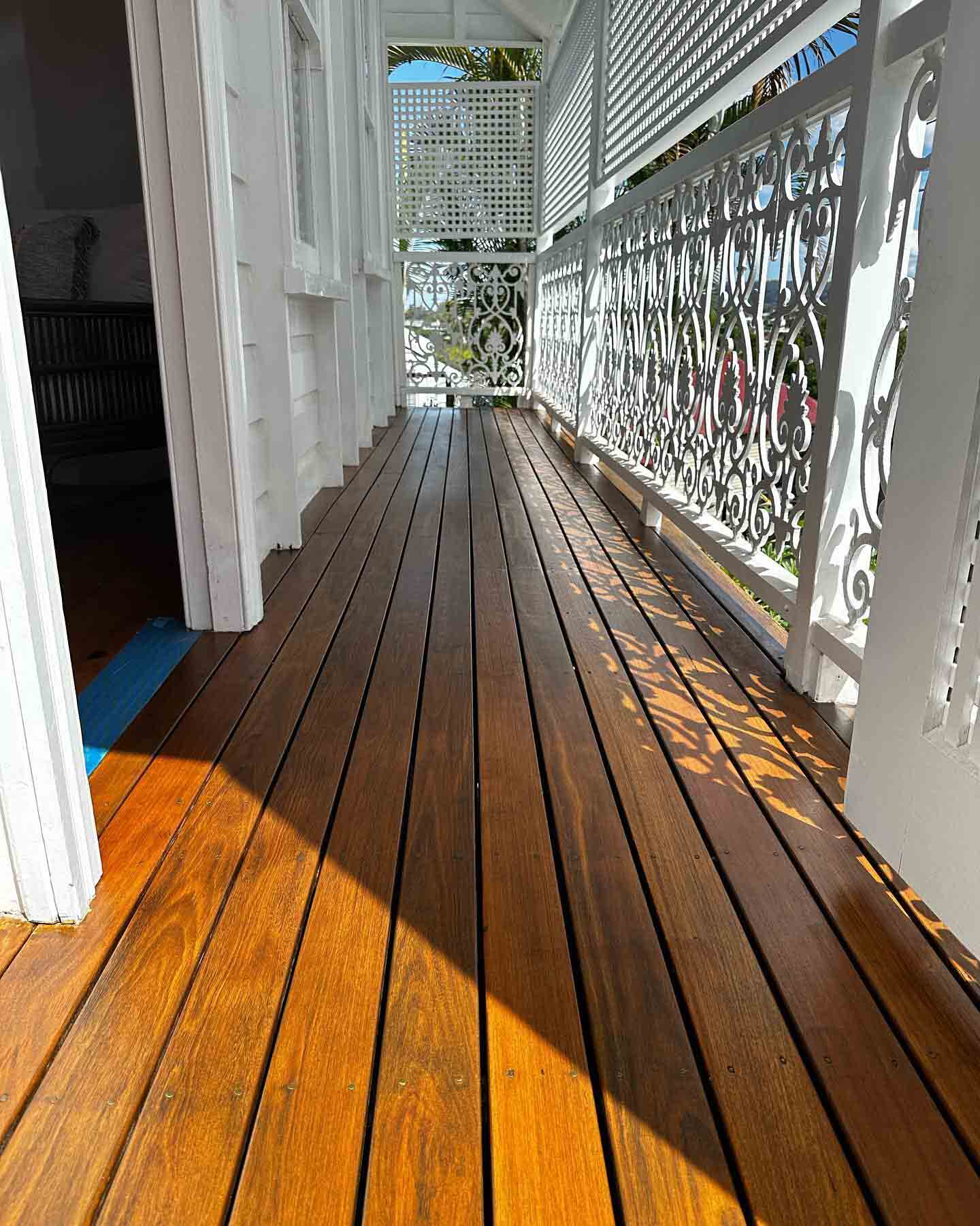 Long narrow oiled timber verandah with ornate white fretwork balustrade