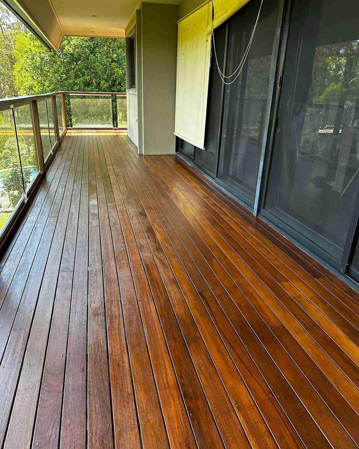 Long oiled timber balcony with glass balustrade beside sliding doors