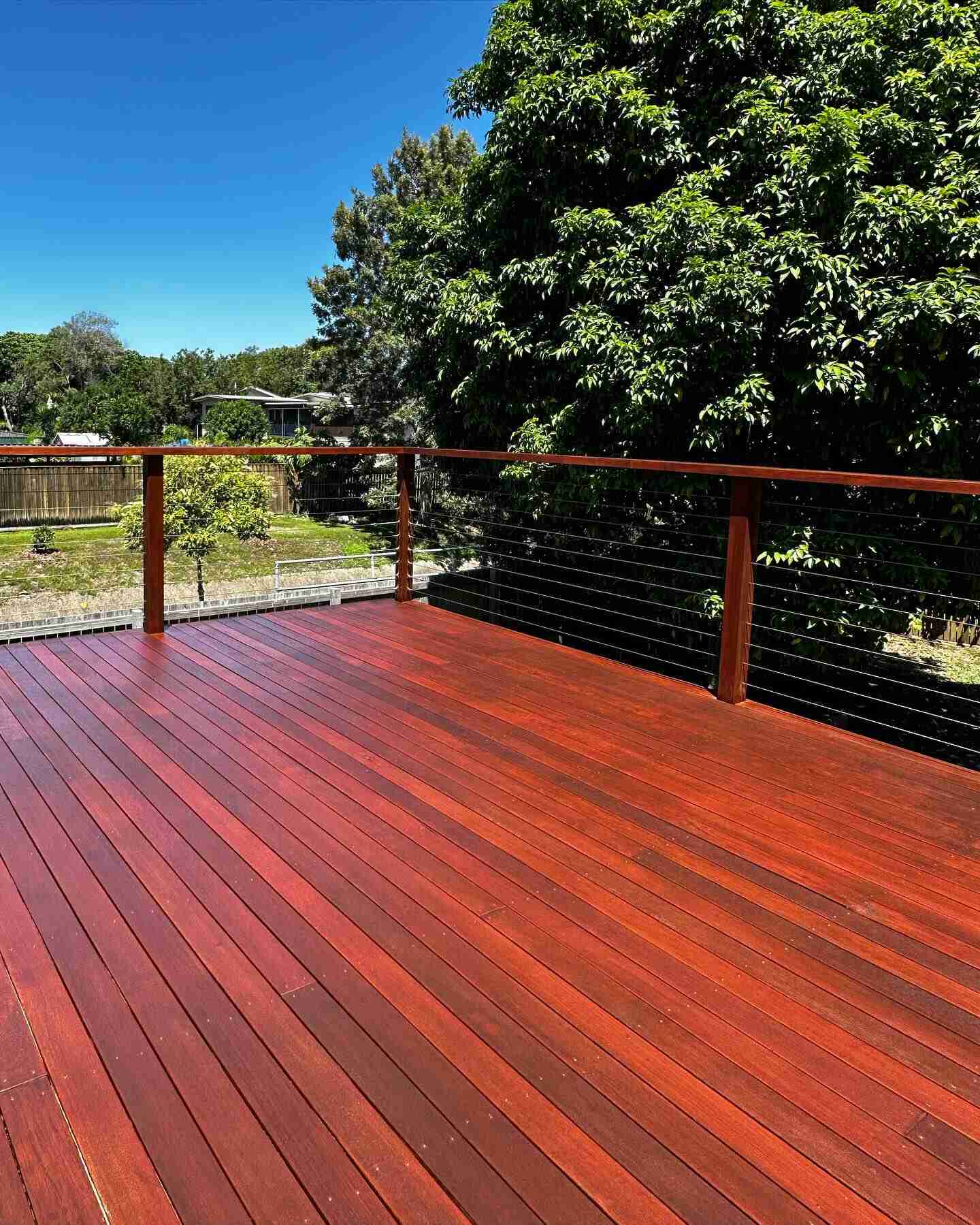 Red-toned oiled timber deck with timber and wire balustrade overlooking a yard