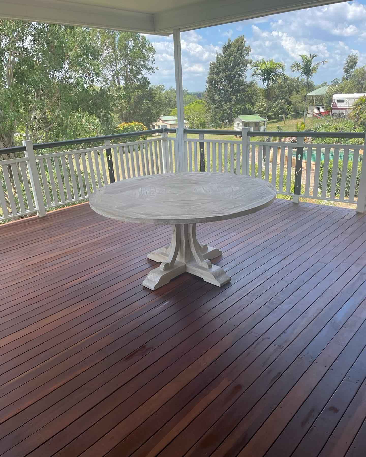 Covered dark timber deck with a round white table, overlooking trees
