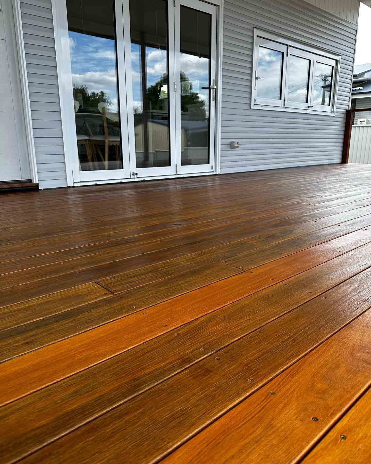 Freshly oiled timber deck outside white French doors on a grey weatherboard house