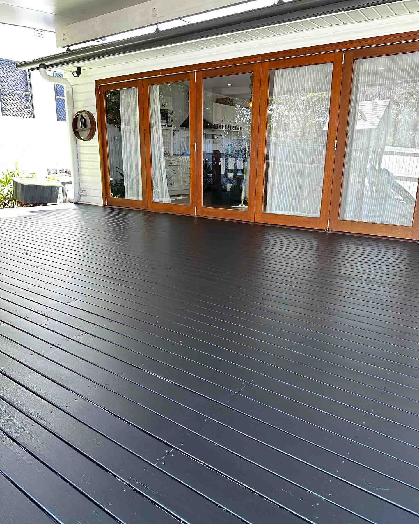Black-stained deck under a patio beside timber-framed bi-fold doors