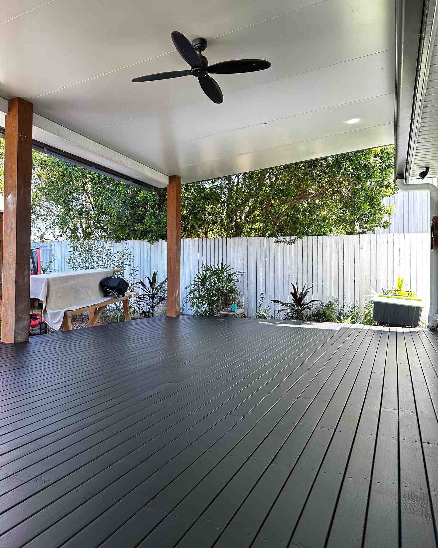 Black-stained deck under a patio roof with timber posts and a white fence