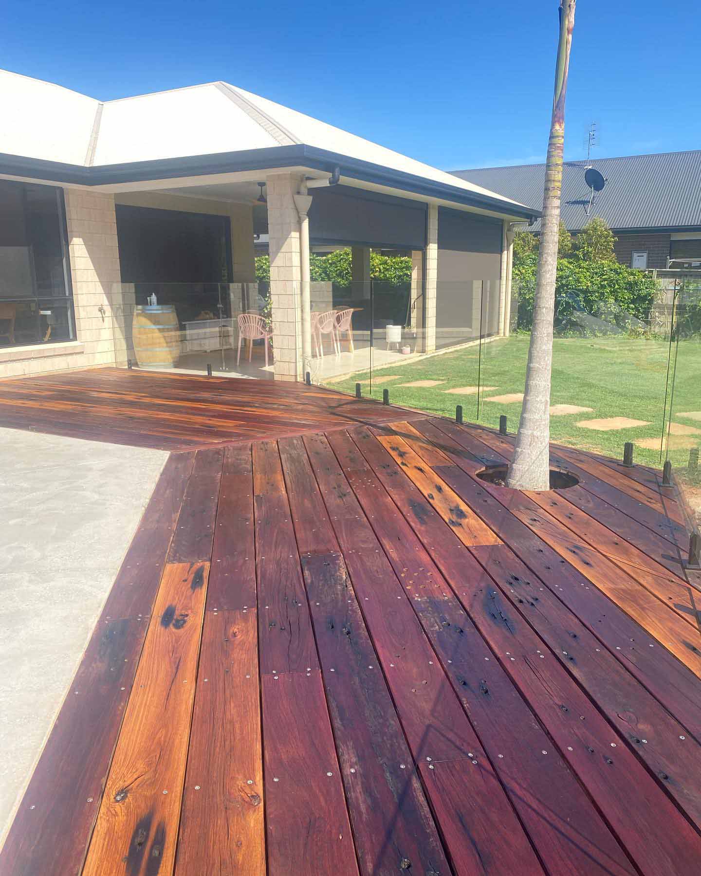 Oiled timber pool deck with dark marks in the boards, built around a palm tree