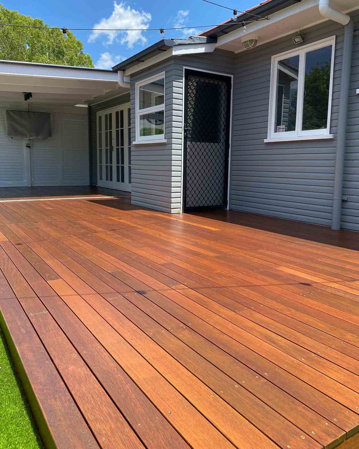 Freshly oiled timber deck outside a grey weatherboard house with a security door