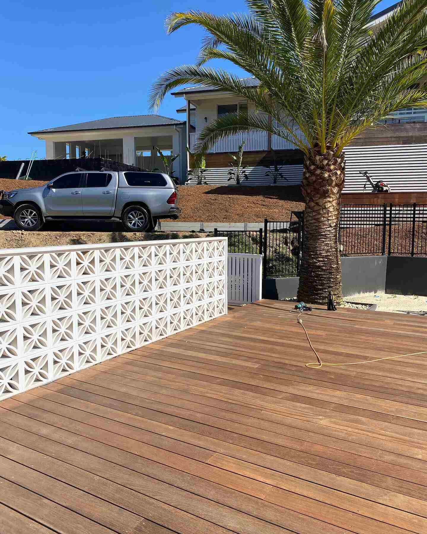 Freshly sanded timber deck beside a white breeze-block wall and palm tree