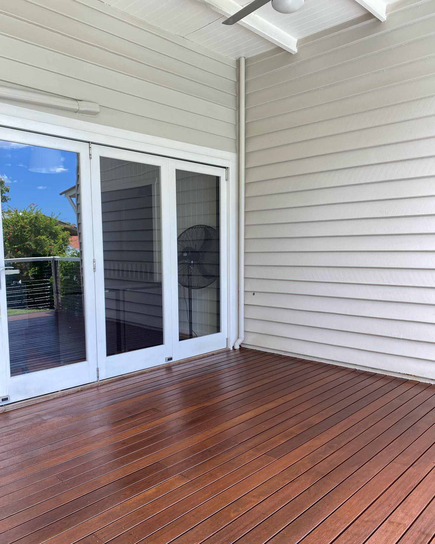 Oiled timber deck outside white French doors on a white weatherboard house