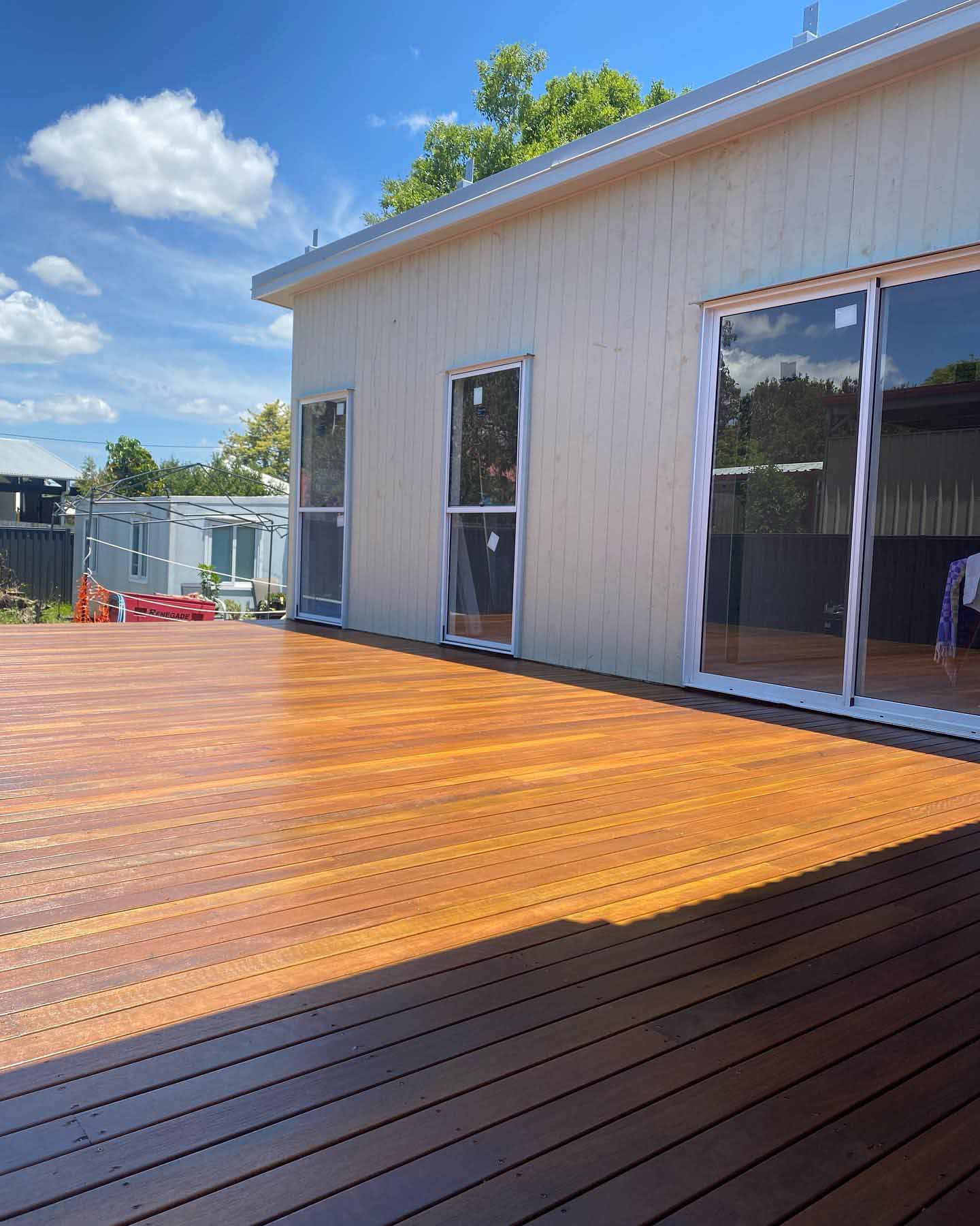Freshly oiled timber deck beside a white clad building with sliding doors