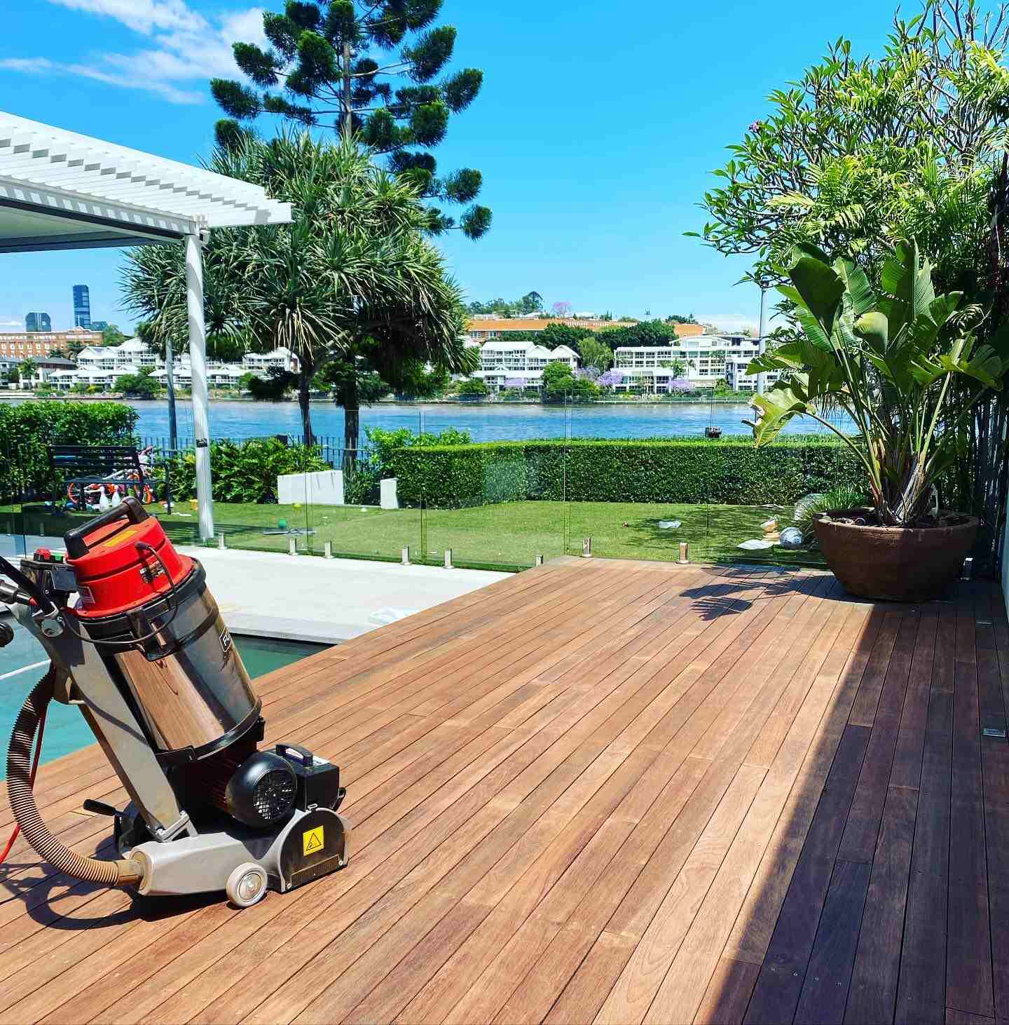 Timber deck mid-sanding with a sanding machine on it, overlooking a river
