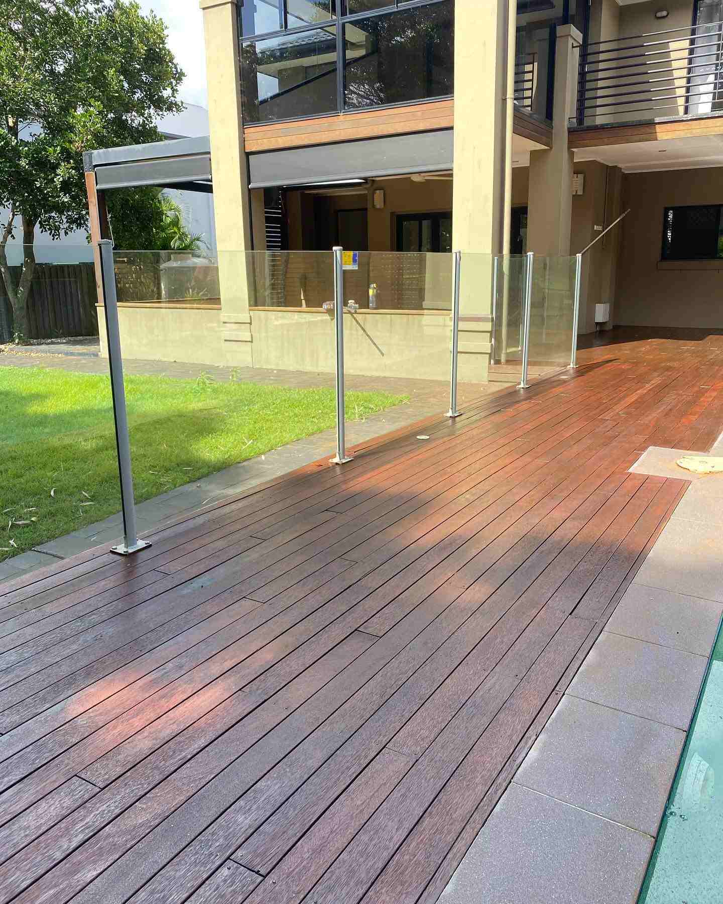 Oiled timber pool deck with glass fencing below a two-storey house