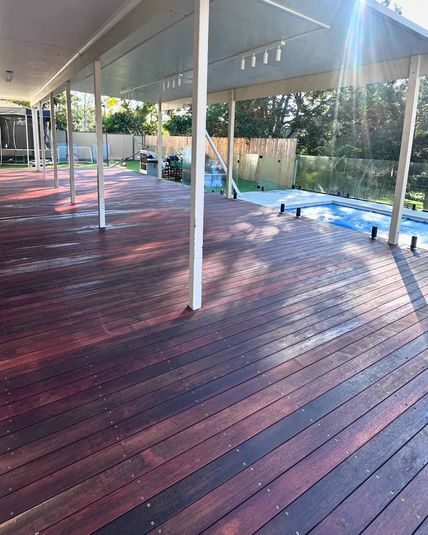Glossy oiled timber deck under a white roof beside a glass-fenced pool