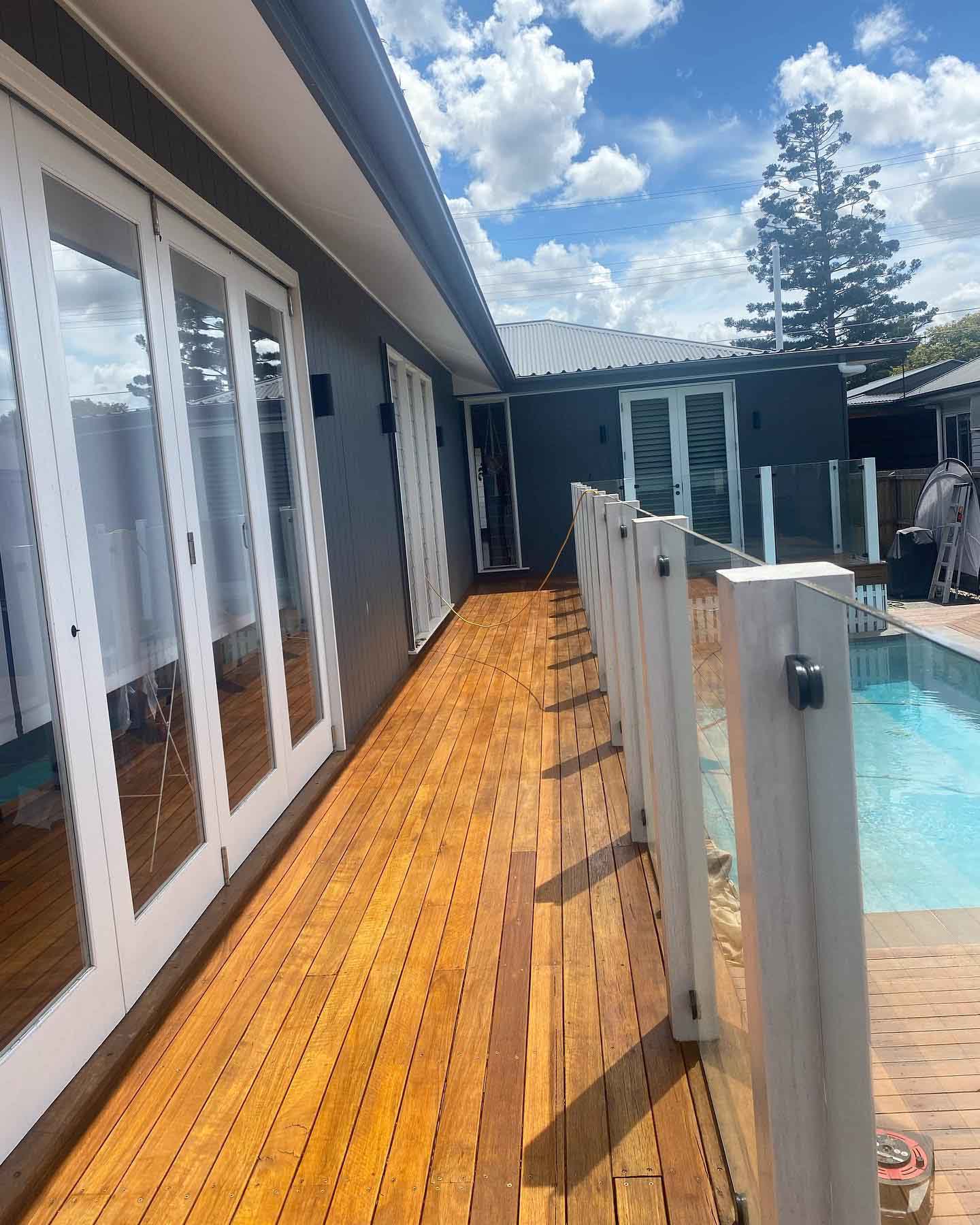 Narrow oiled timber deck between white French doors and a glass pool fence