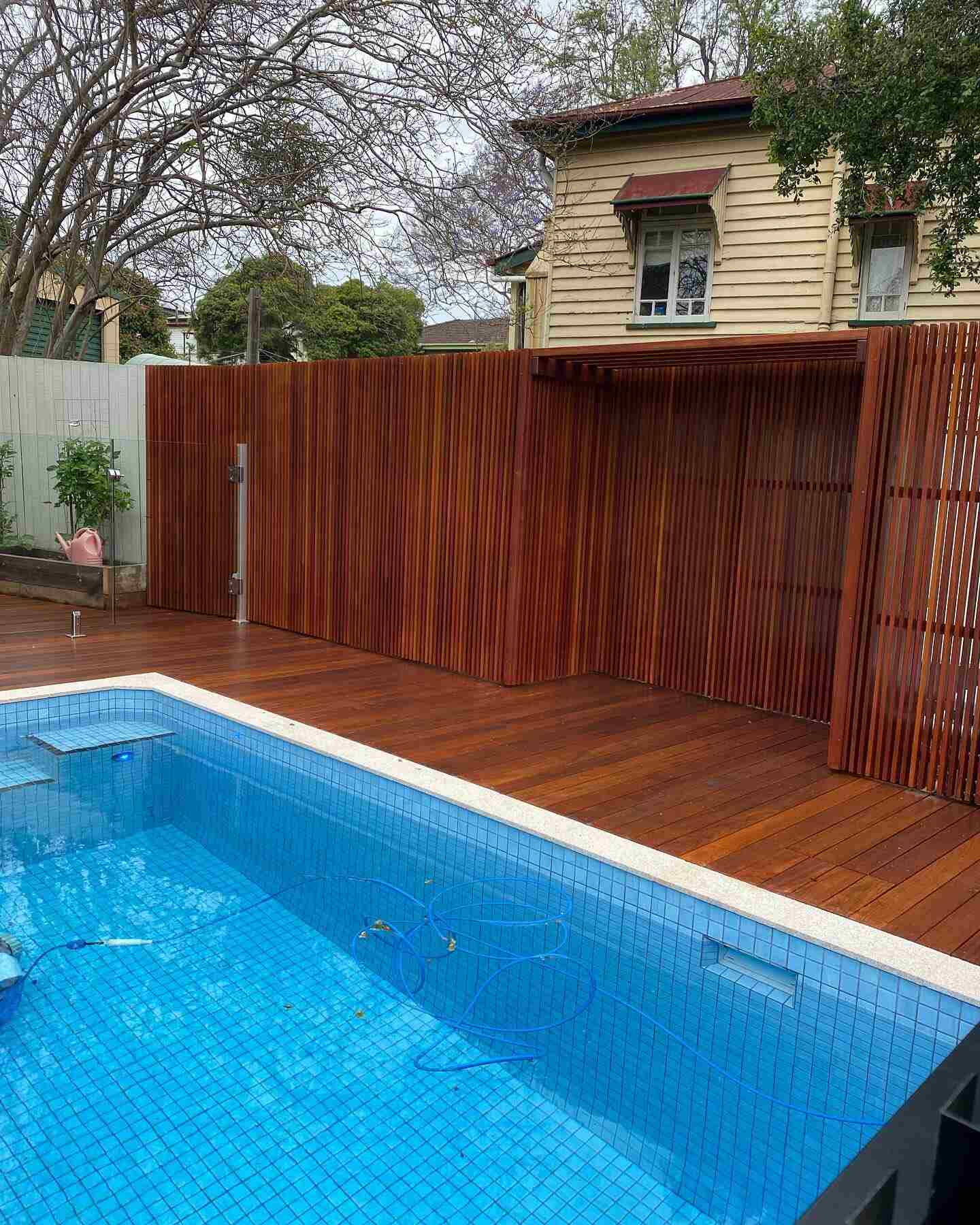 Oiled timber pool deck with a tall timber slat screen beside a tiled pool