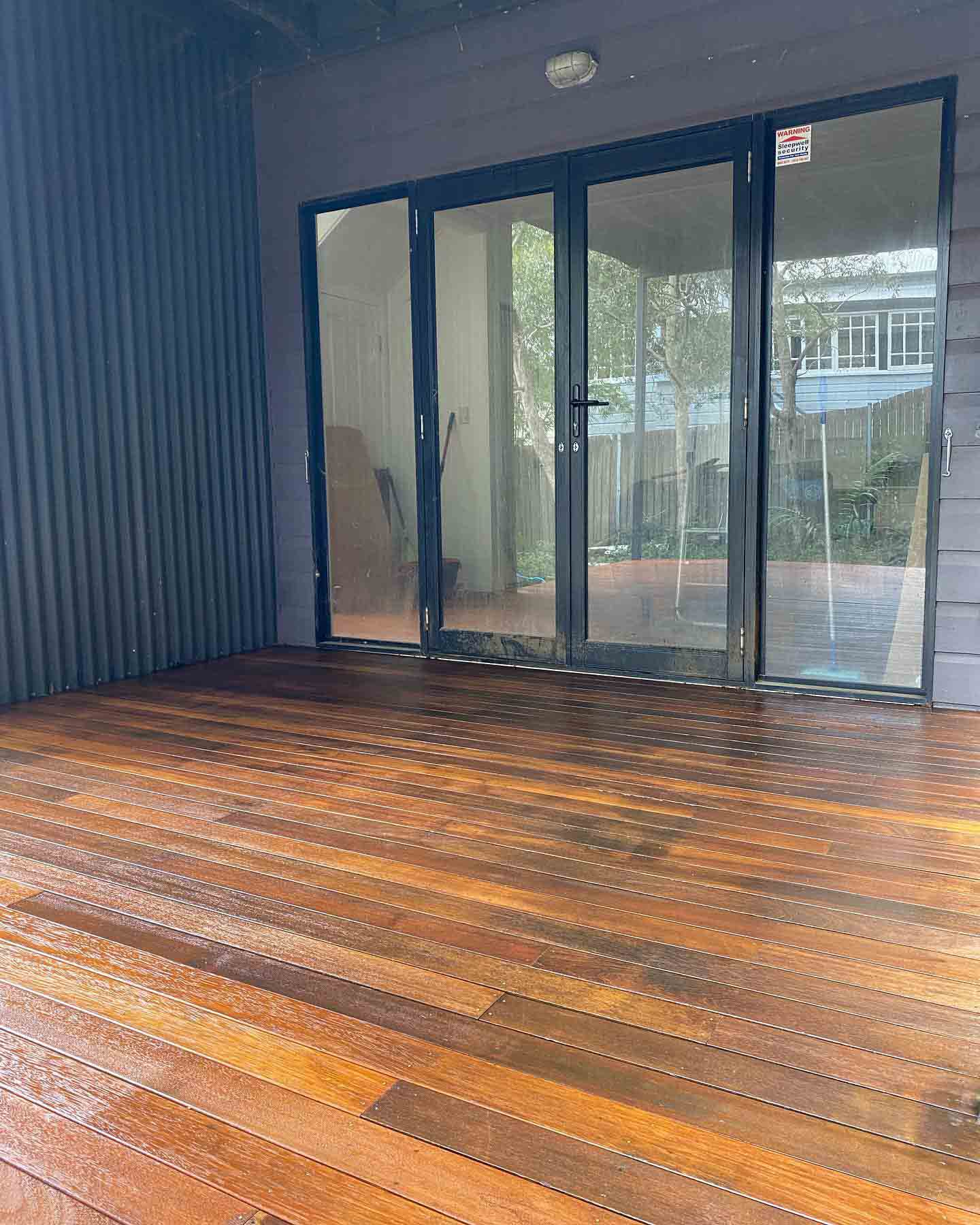 Oiled timber deck in front of black-framed glass doors and dark cladding