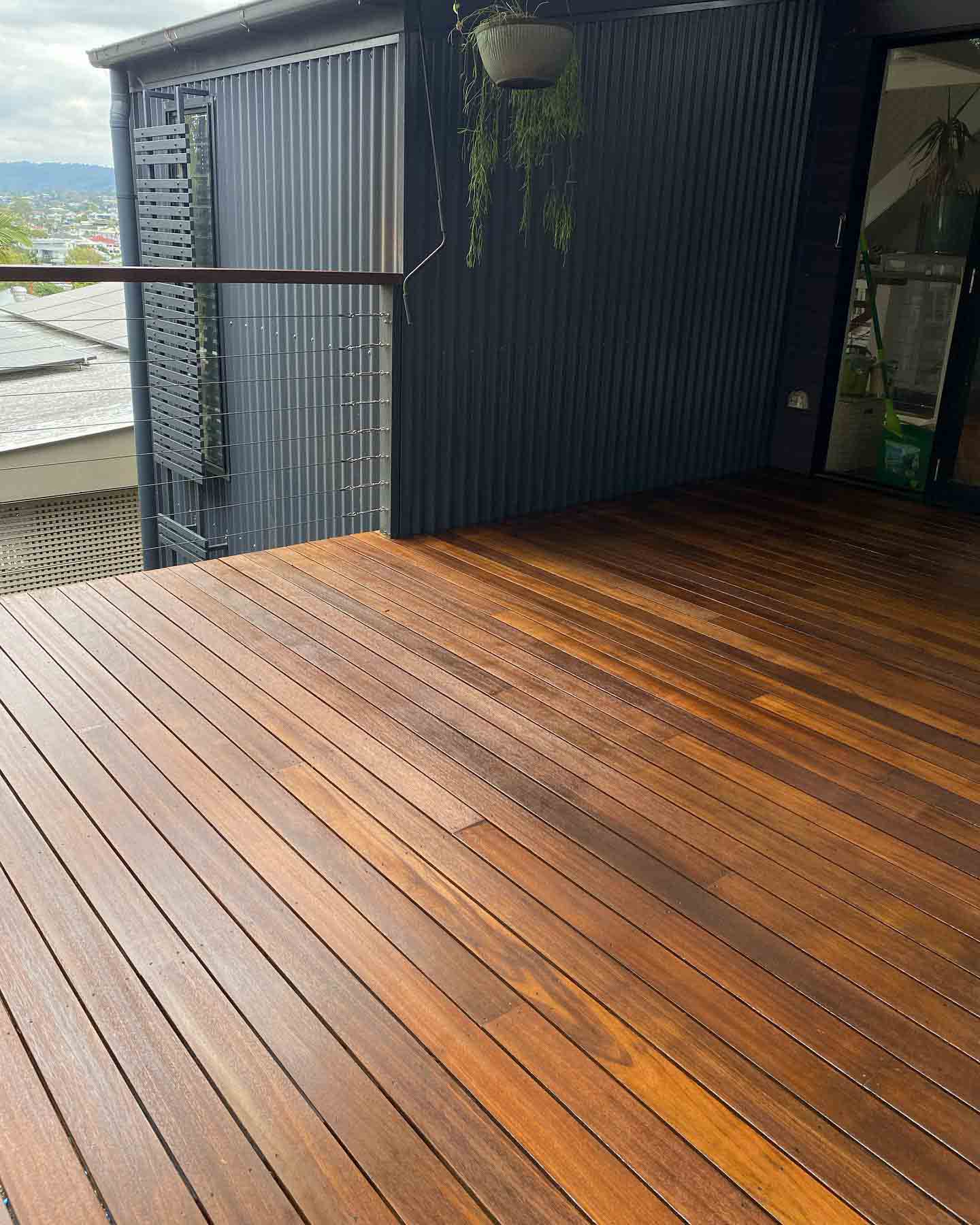 Oiled timber balcony deck beside dark cladding, with hills in the distance