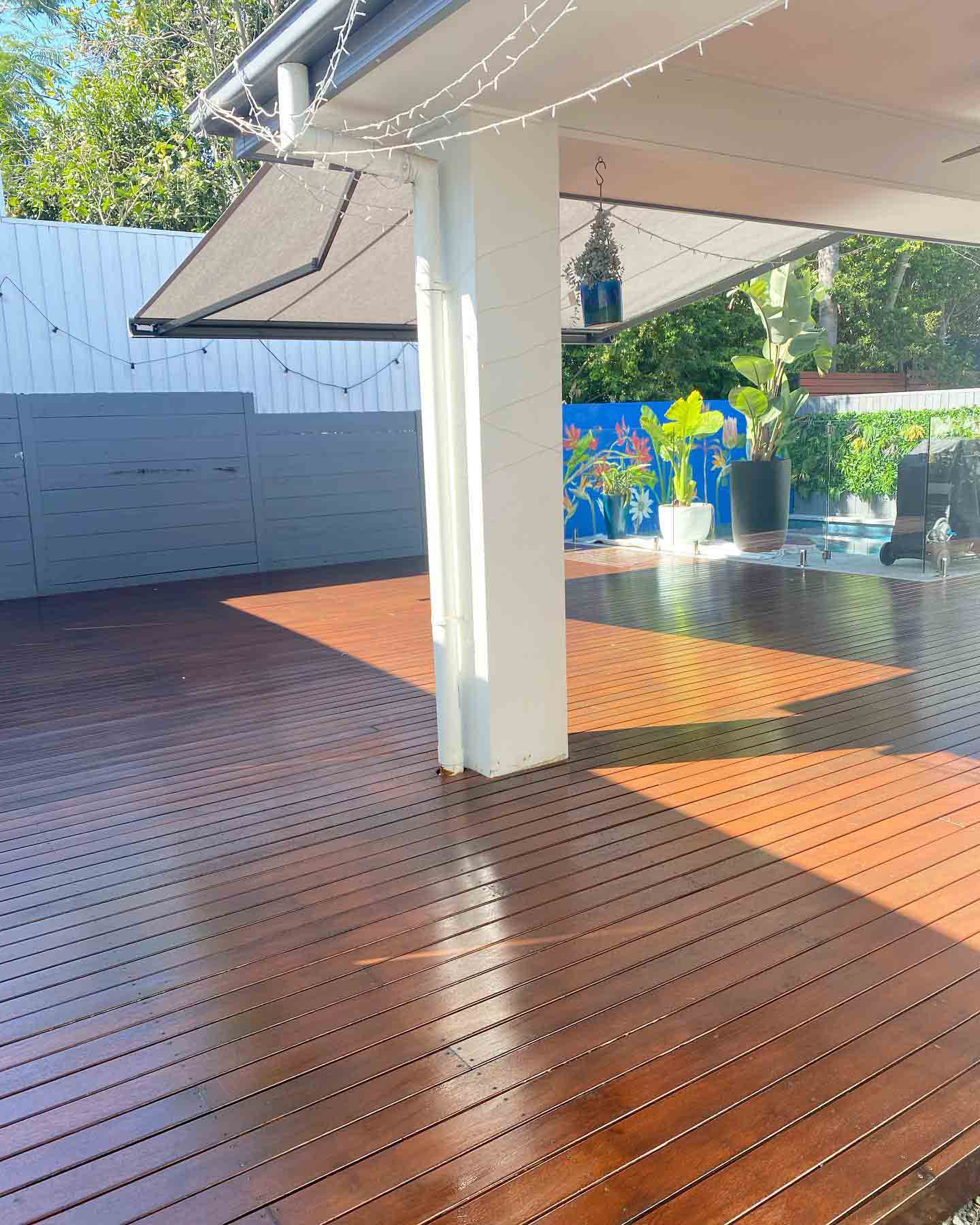 Glossy oiled timber deck around a white post under a patio awning