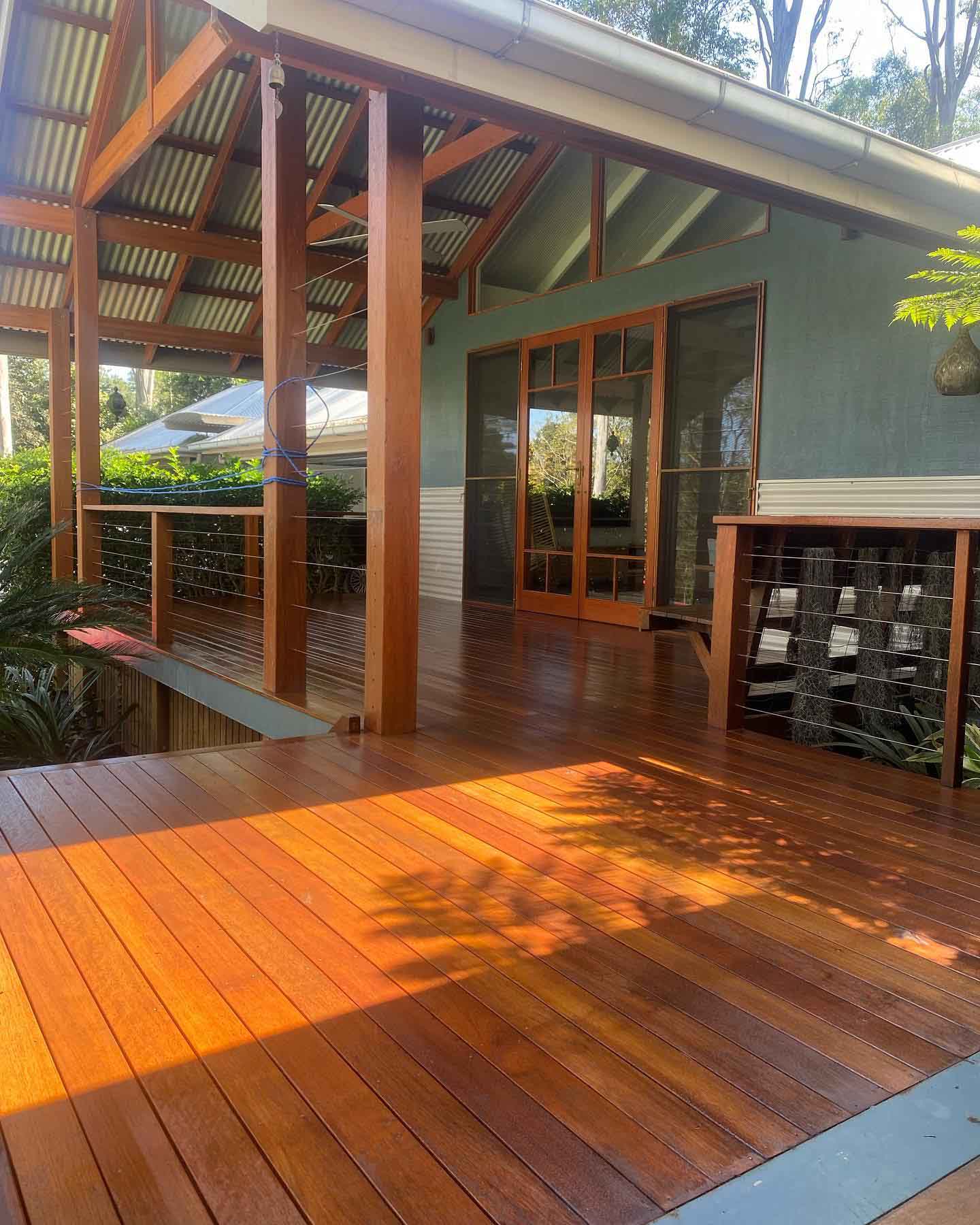 Sunlit oiled timber deck under a timber-framed roof with wire balustrade
