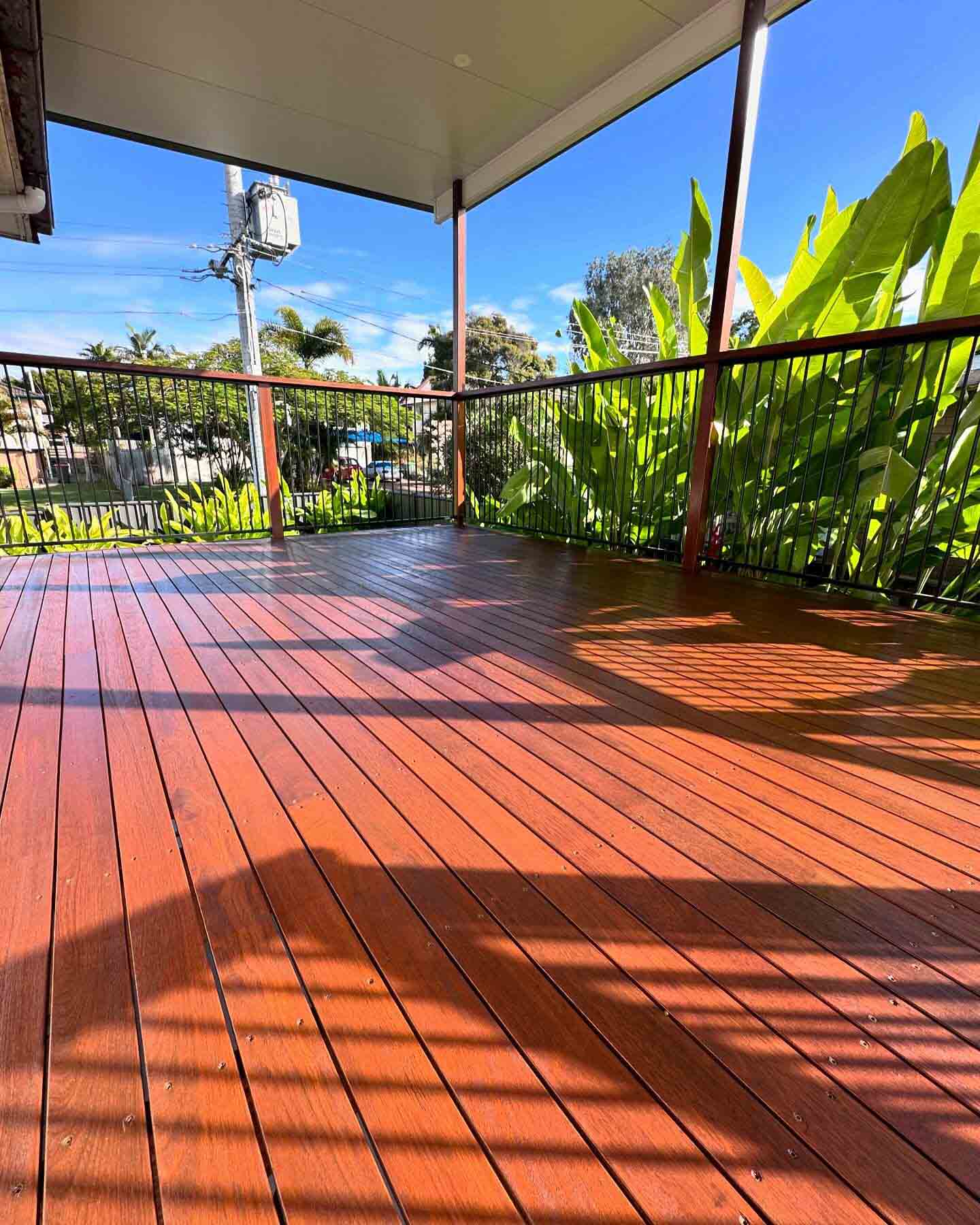Freshly oiled timber deck in afternoon sun with tropical plants along the railing