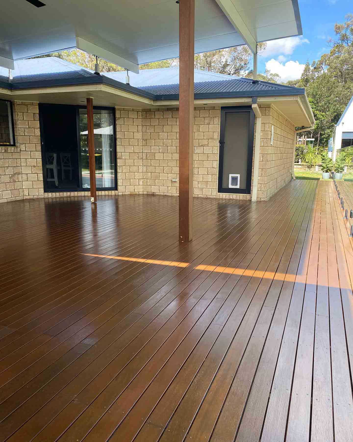 Oiled timber deck under a raised roof beside a sandstone-coloured house