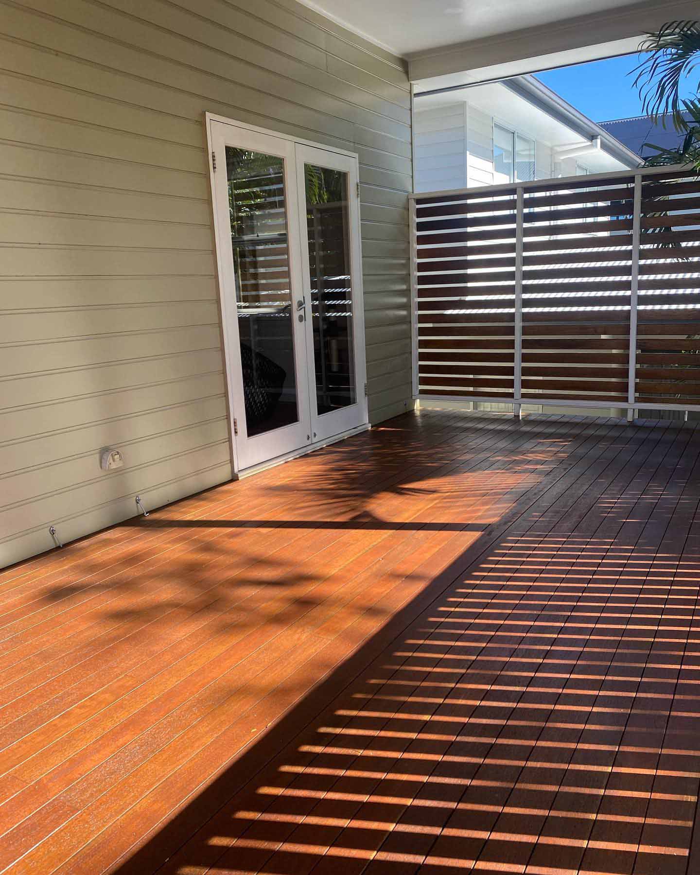 Oiled timber deck with a slatted privacy screen beside cream weatherboards