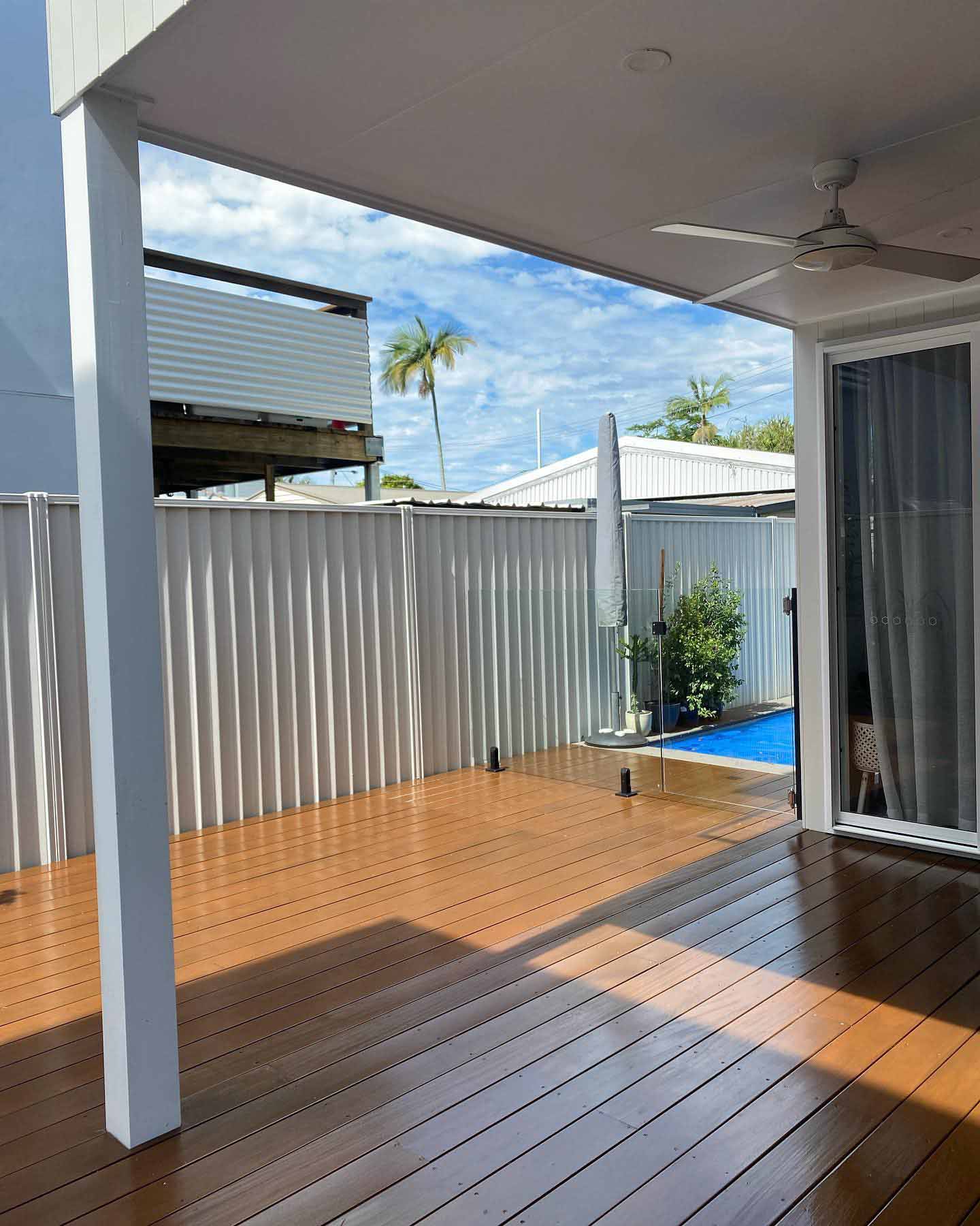 Brown-coated deck under a patio beside a pool, with steel fencing