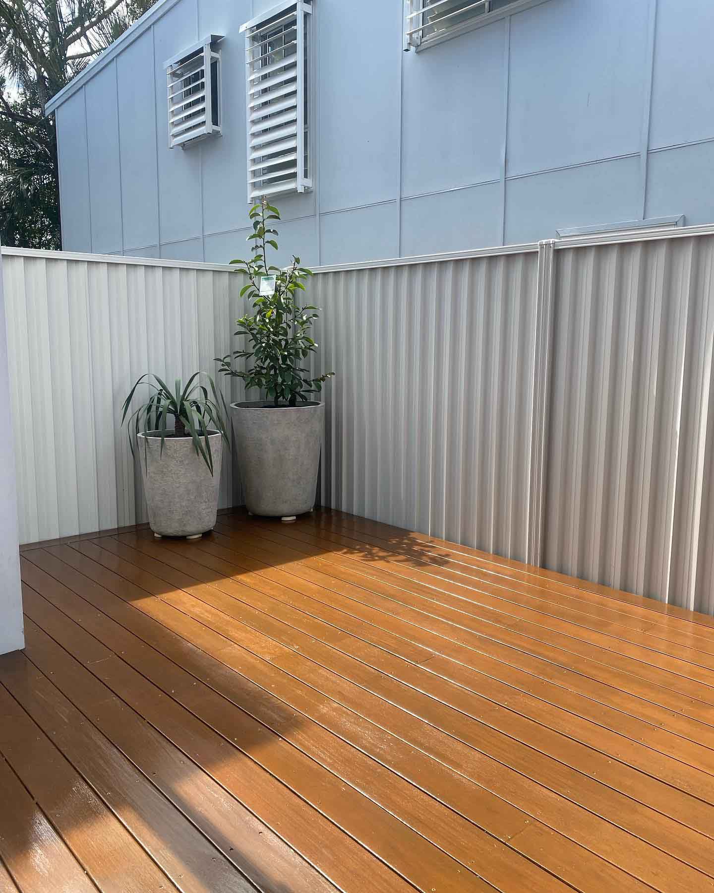 Freshly coated deck in a courtyard with steel fencing and pot plants