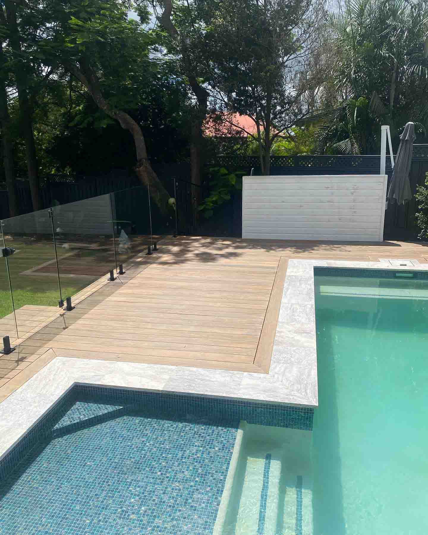 Sanded timber deck around a tiled pool with glass fencing