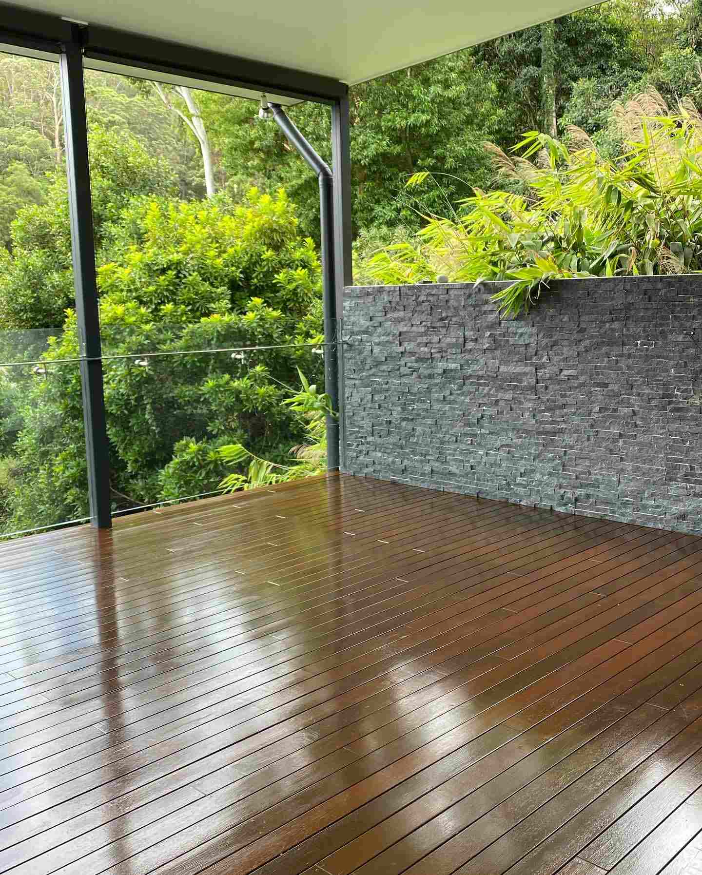 Glossy oiled timber deck with a stacked stone wall and bushland view