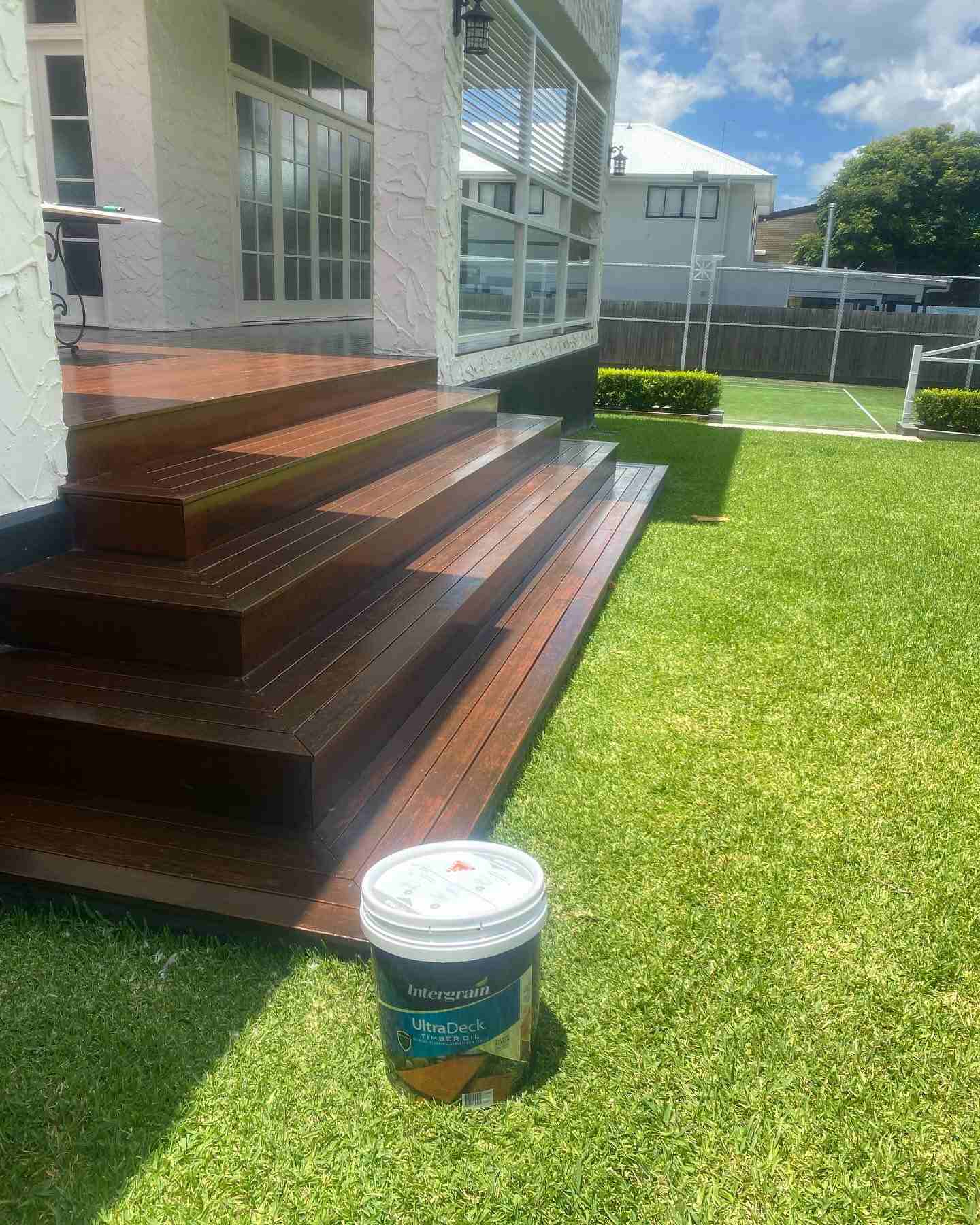 Wide oiled timber steps down to a lawn, with a tin of finish beside them