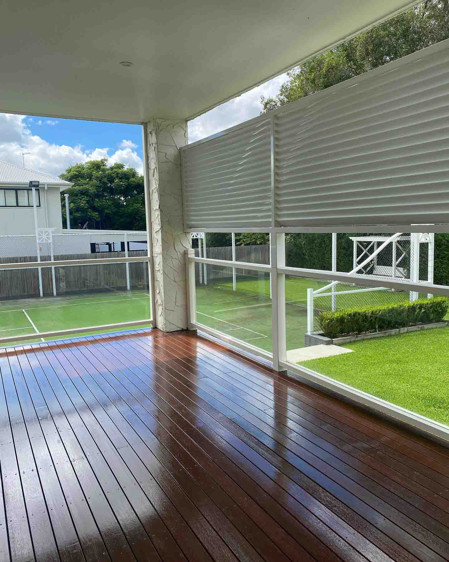 Glossy covered timber deck with glass balustrade overlooking a sports court
