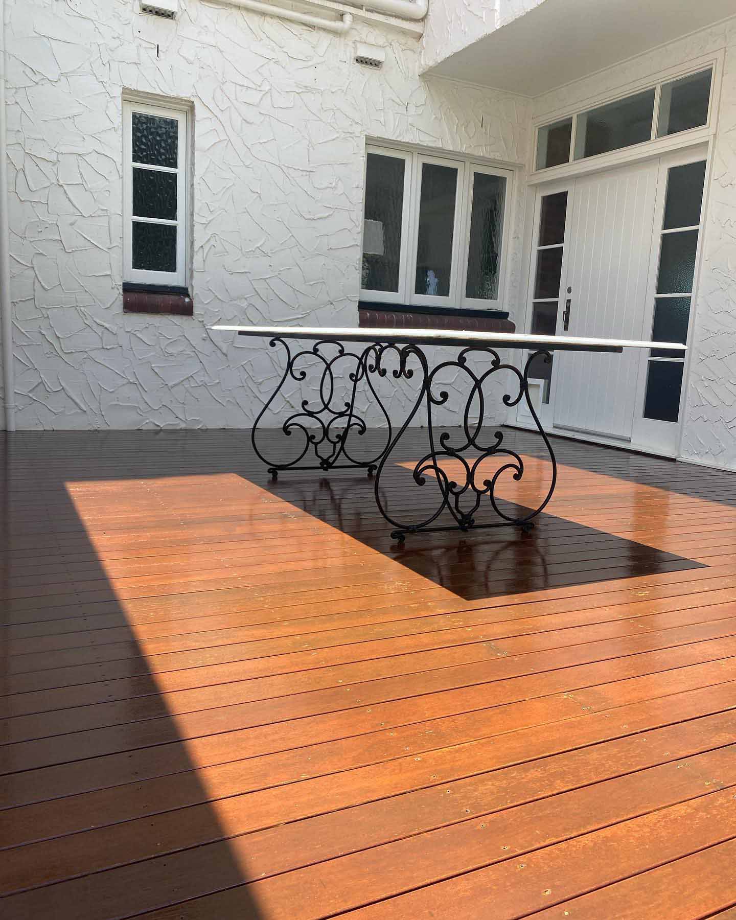 Oiled timber deck with a wrought-iron table beside a white rendered house