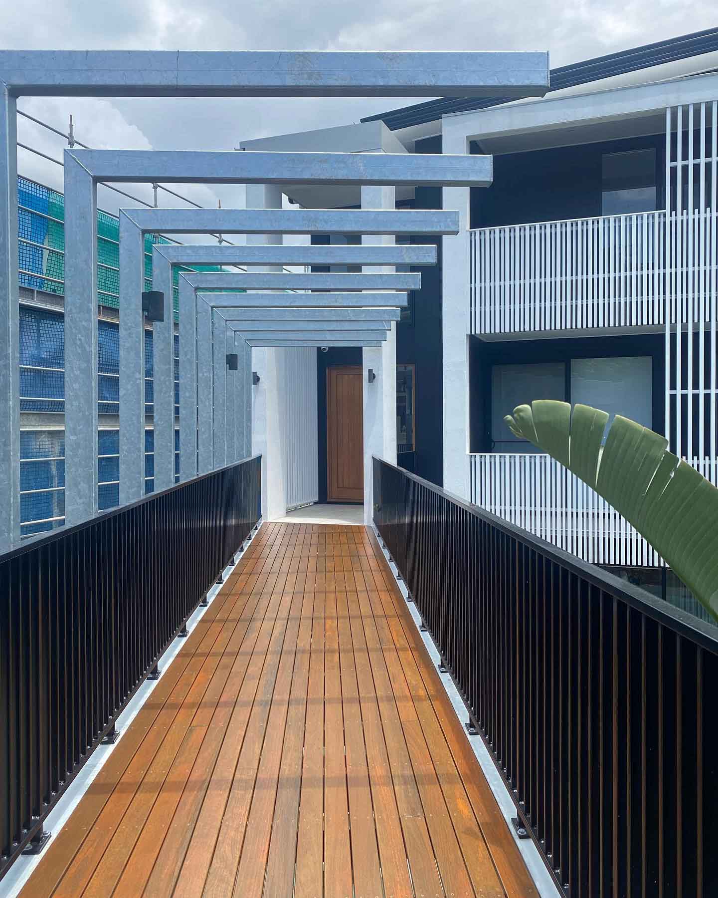 Timber boardwalk entry with black balustrade under a pergola
