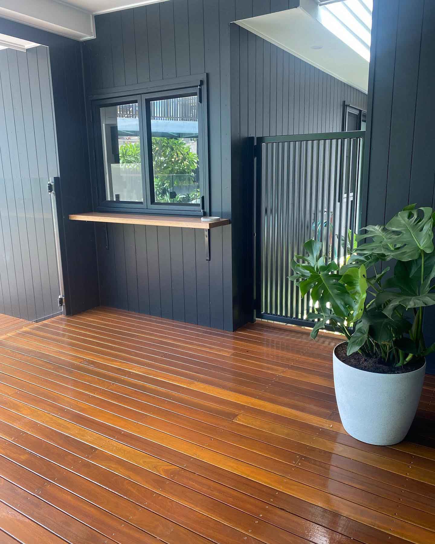 Oiled timber deck with a potted plant beside dark vertical cladding