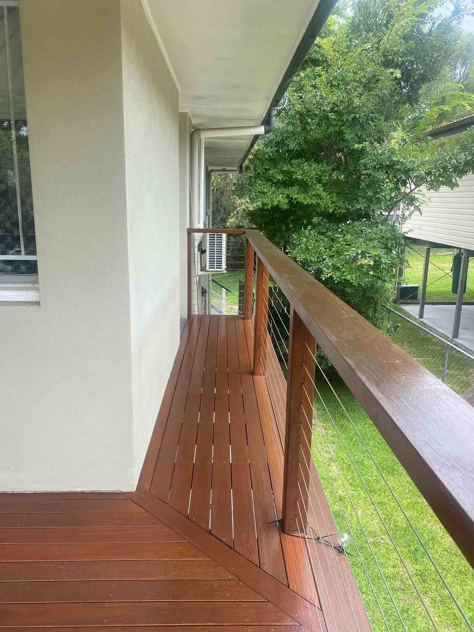 Narrow oiled timber deck along a rendered wall with timber and wire balustrade