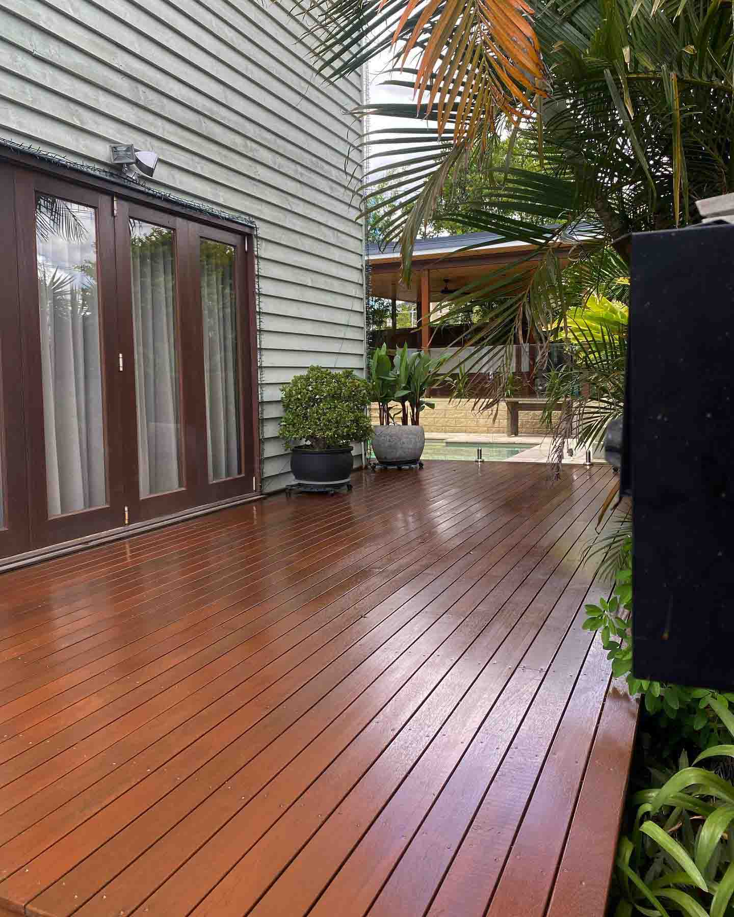 Oiled timber deck beside timber French doors on a grey weatherboard house