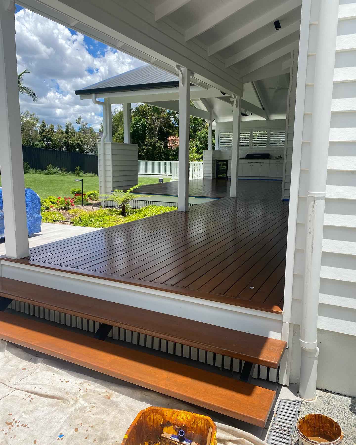 Oiled timber verandah and steps on a white weatherboard house beside a garden