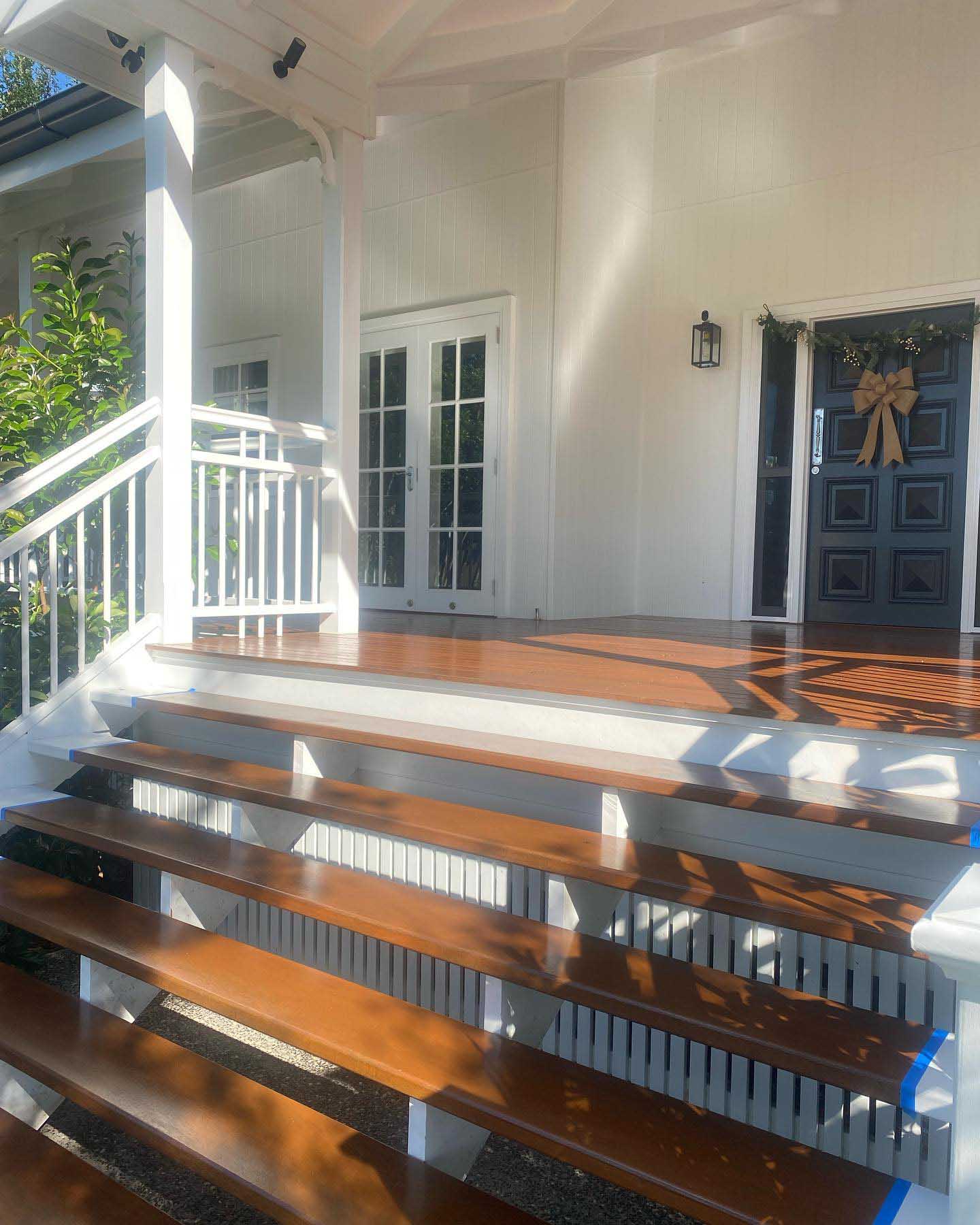 Oiled timber steps and verandah leading to a navy front door