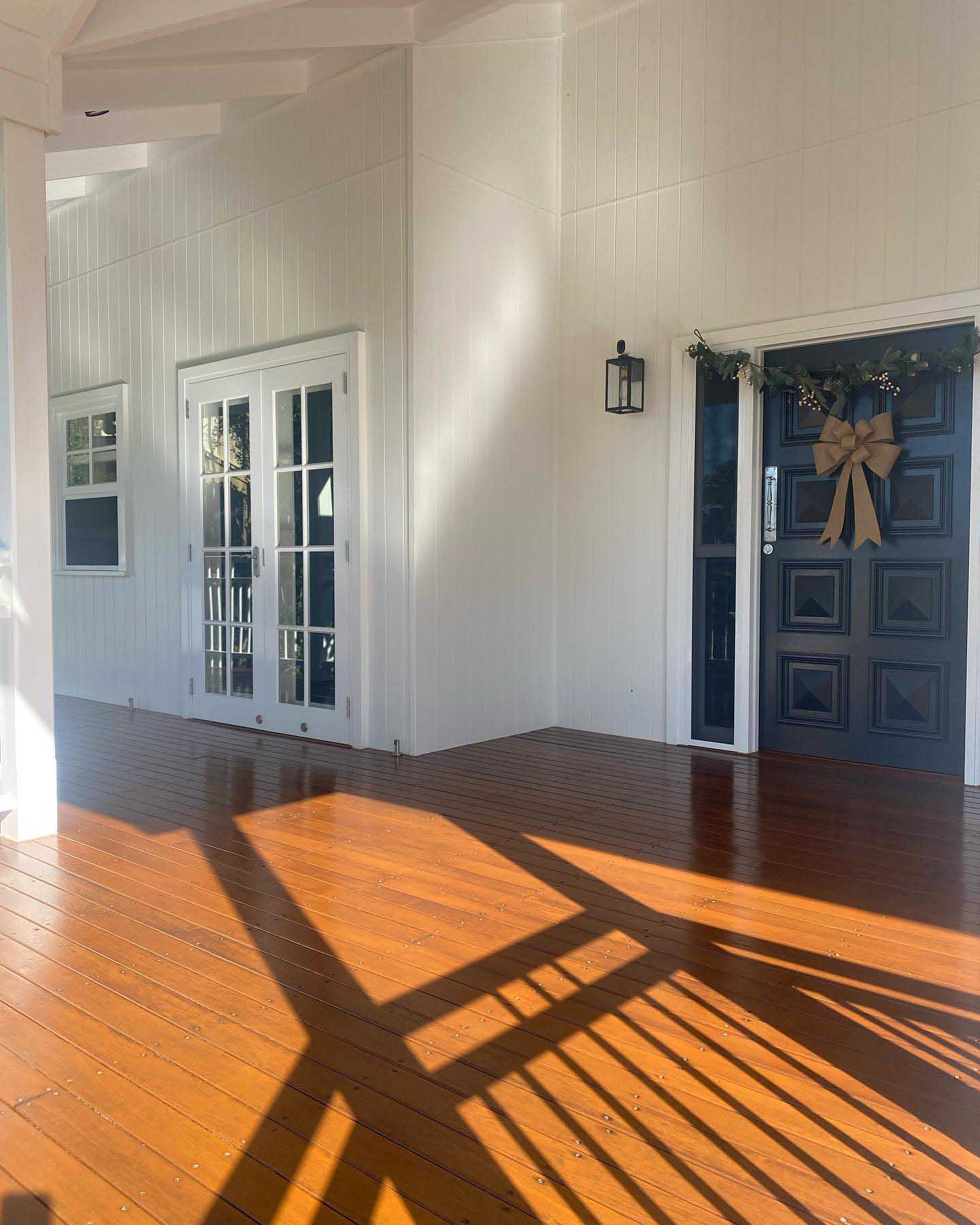 Sunlit oiled timber verandah in front of a navy front door with a wreath