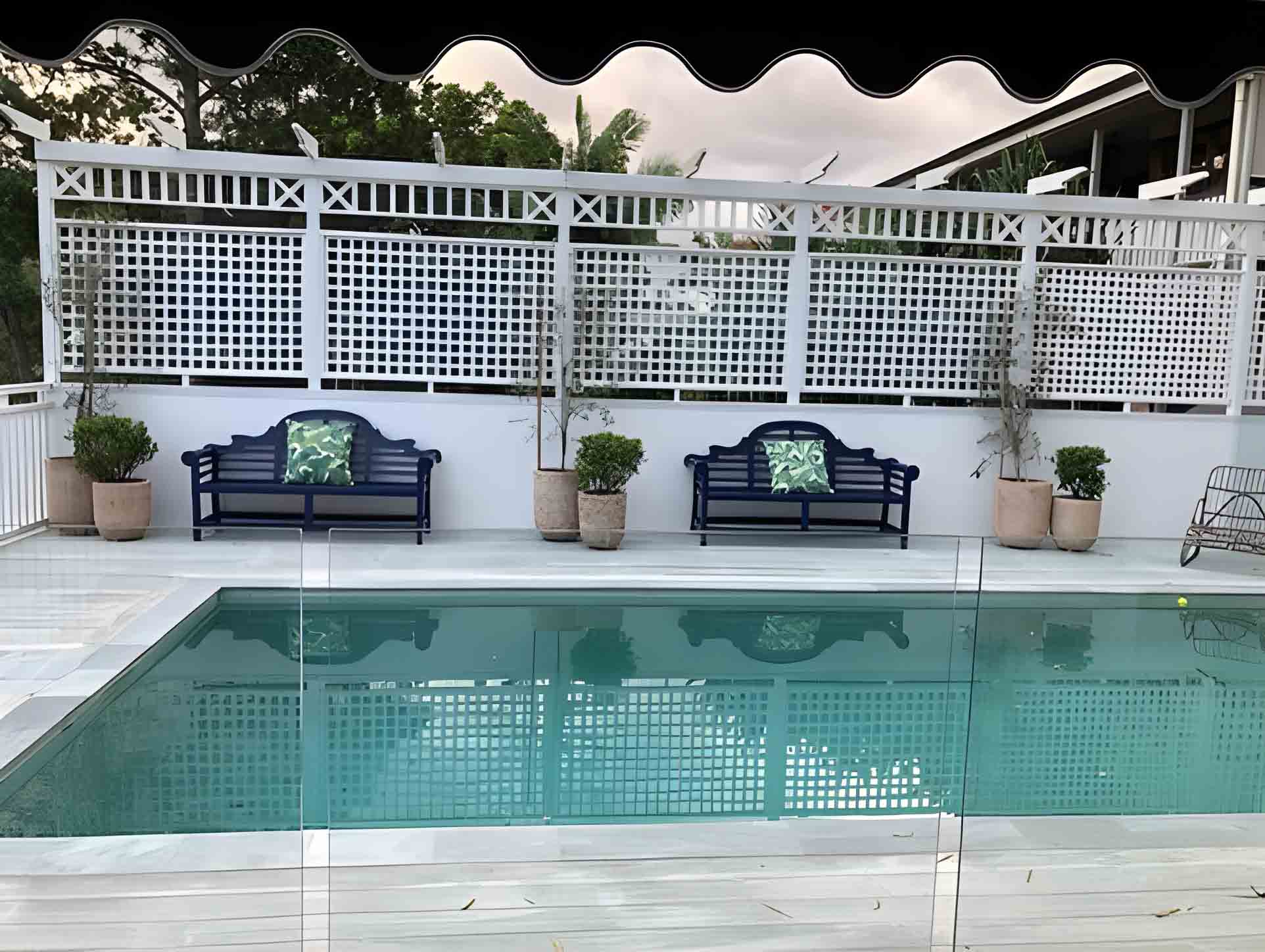 Pool with pale grey decking and a white lattice screen behind two navy benches