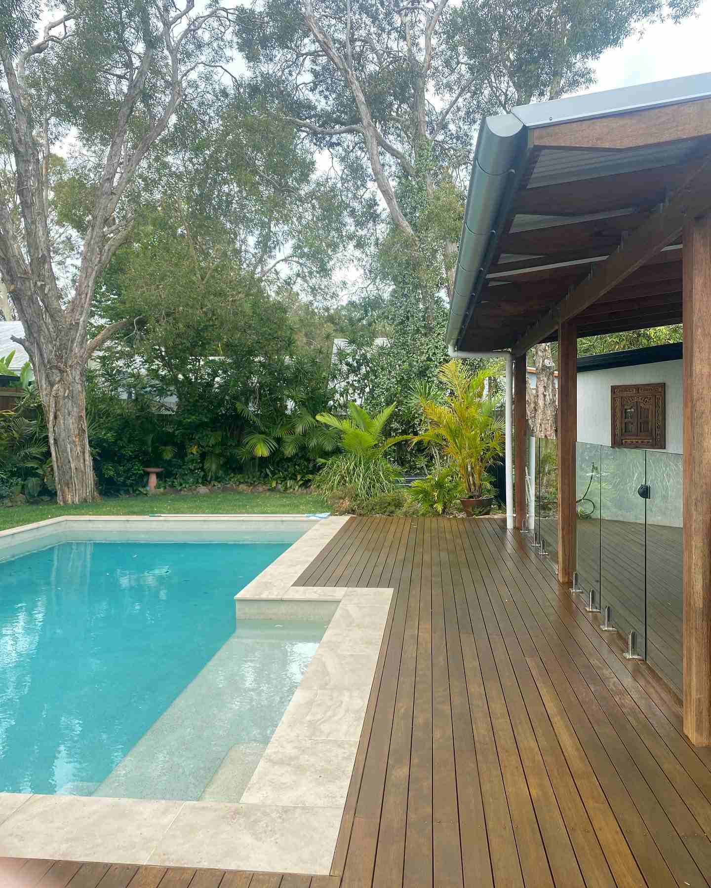 Oiled timber deck beside a pool with a timber-posted shelter and trees