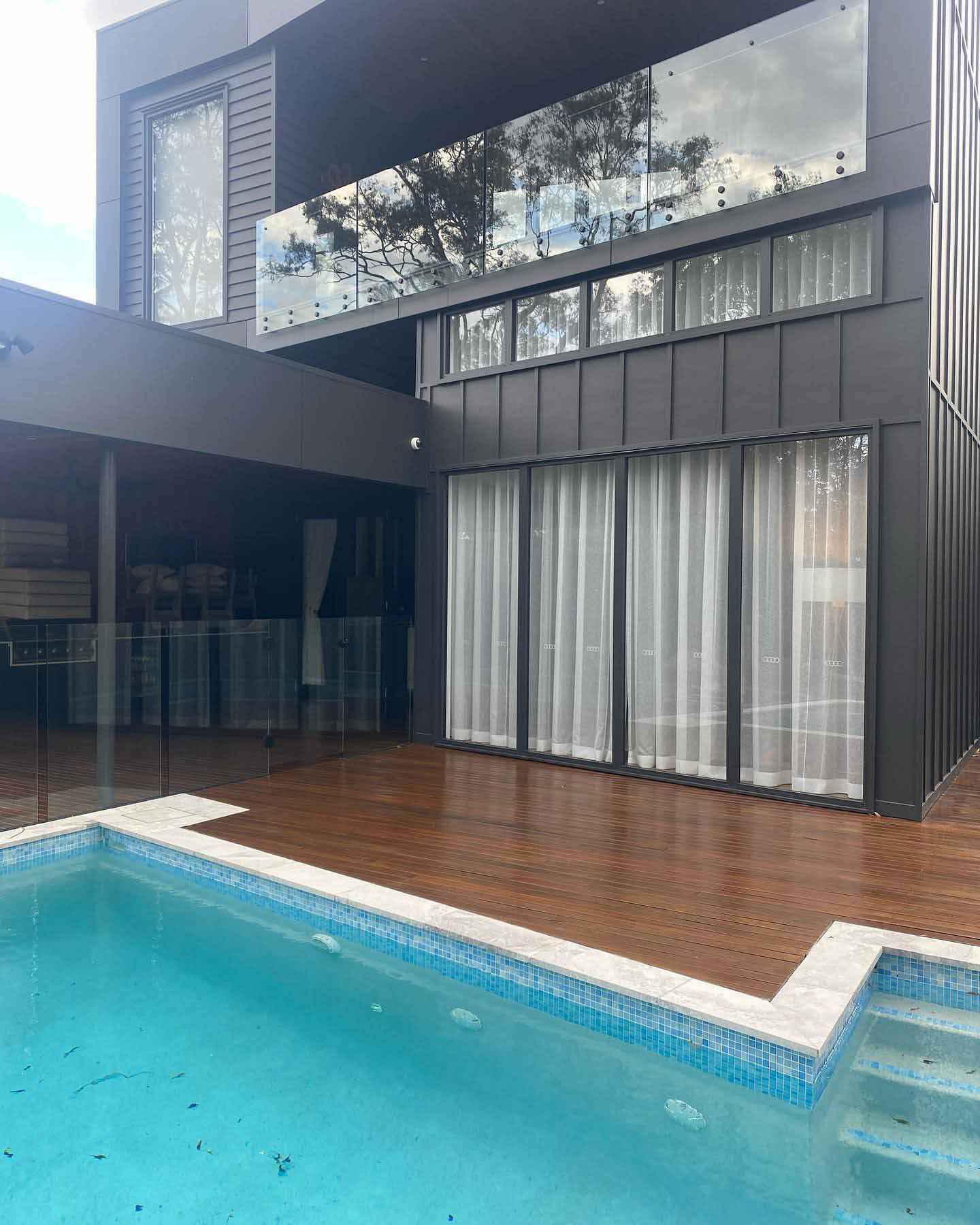 Oiled timber deck around a pool below a modern black two-storey house
