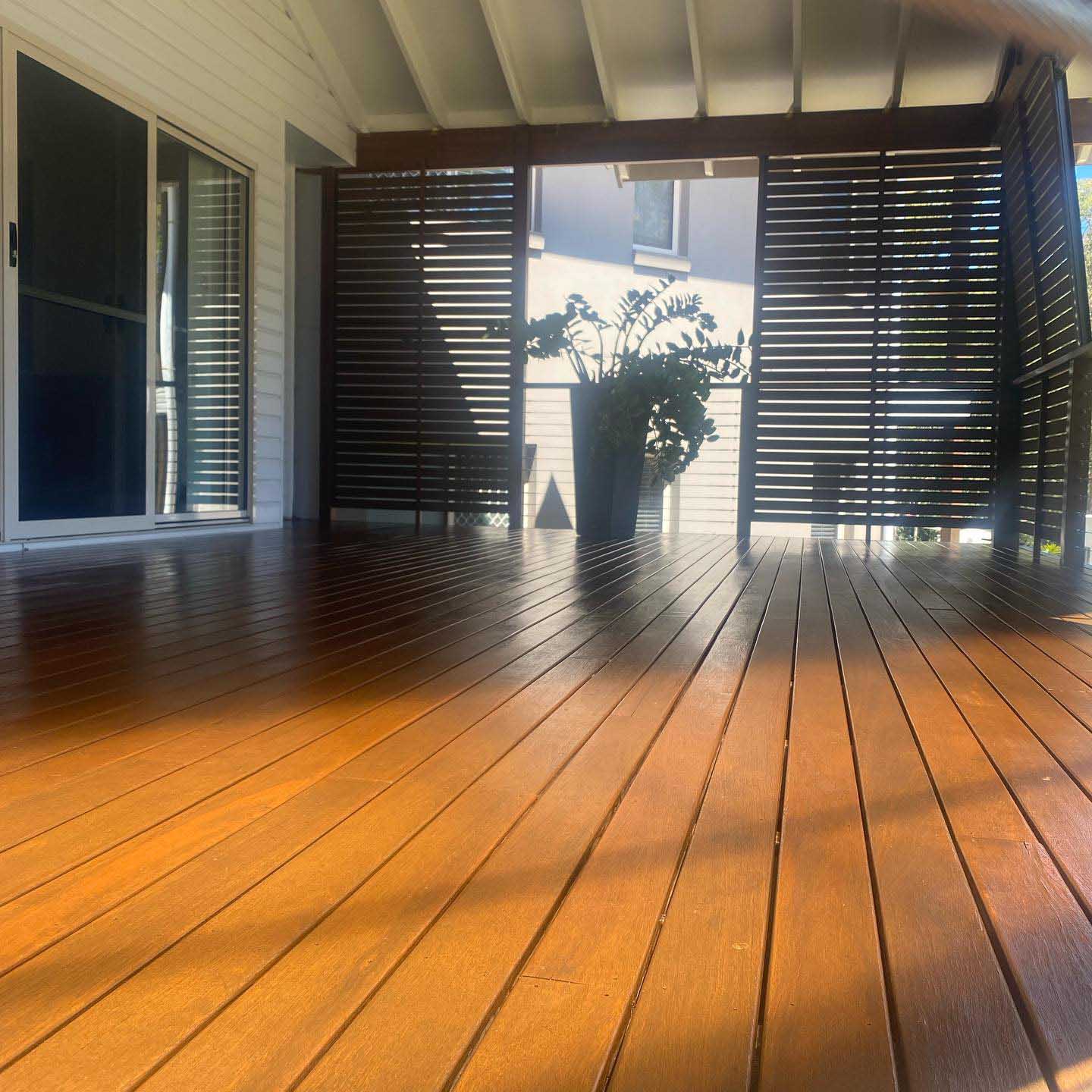 Glossy oiled timber deck with dark slatted screens in golden light
