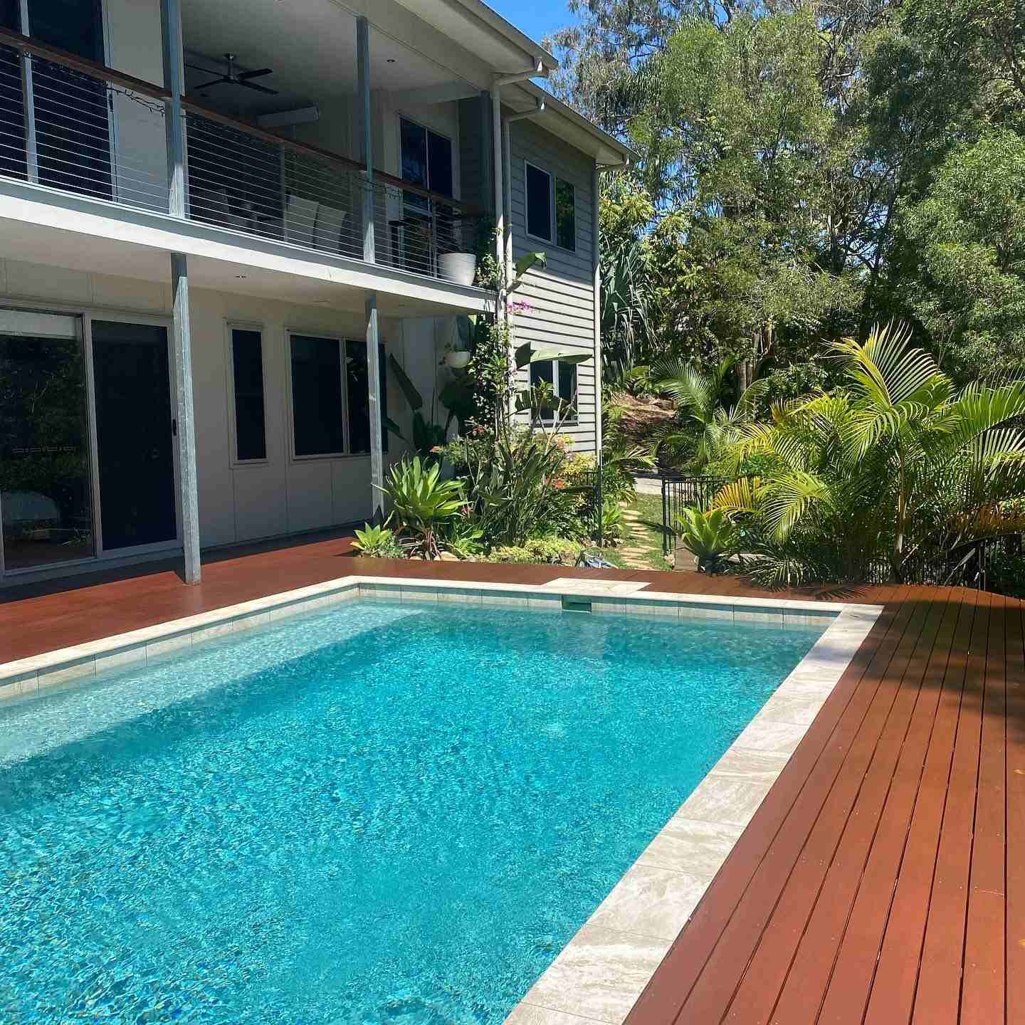 Oiled timber deck around a tiled pool beside a two-storey house