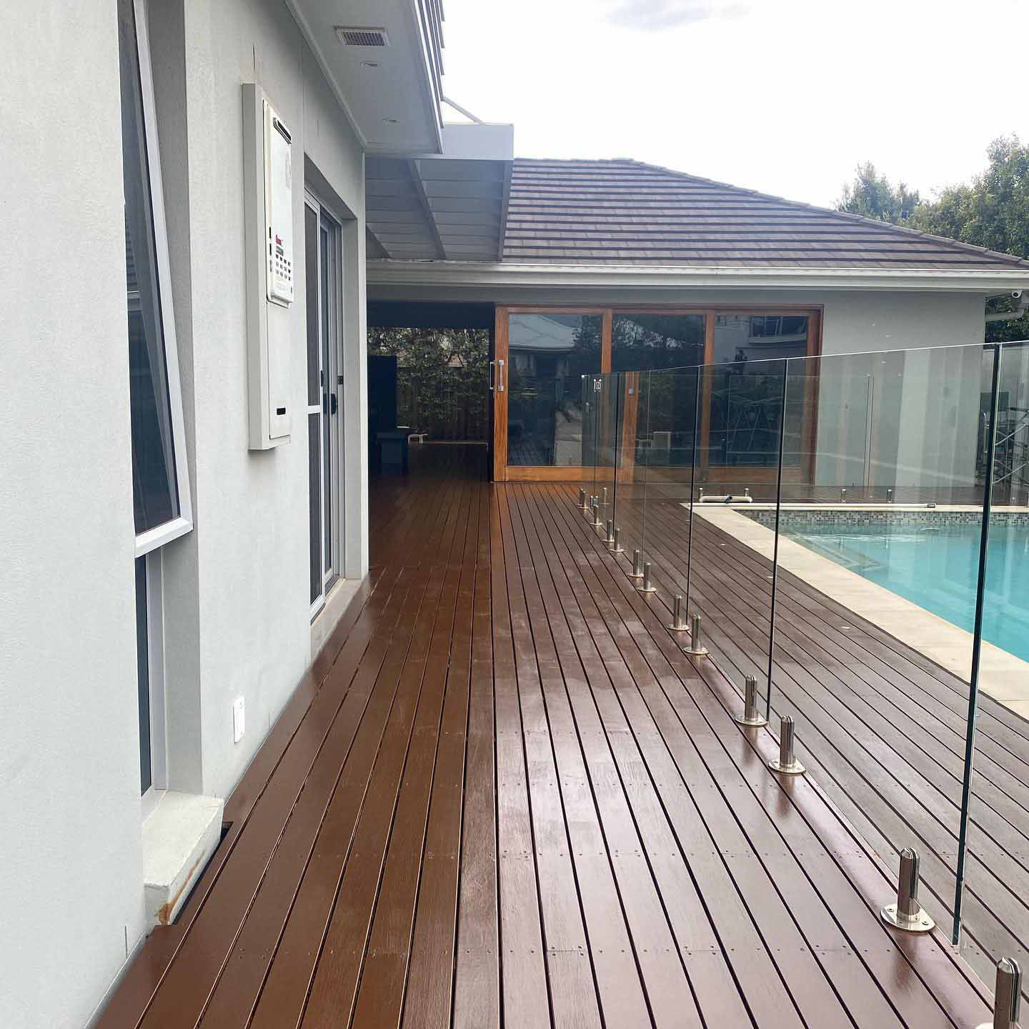 Oiled timber deck along glass pool fencing beside a rendered house