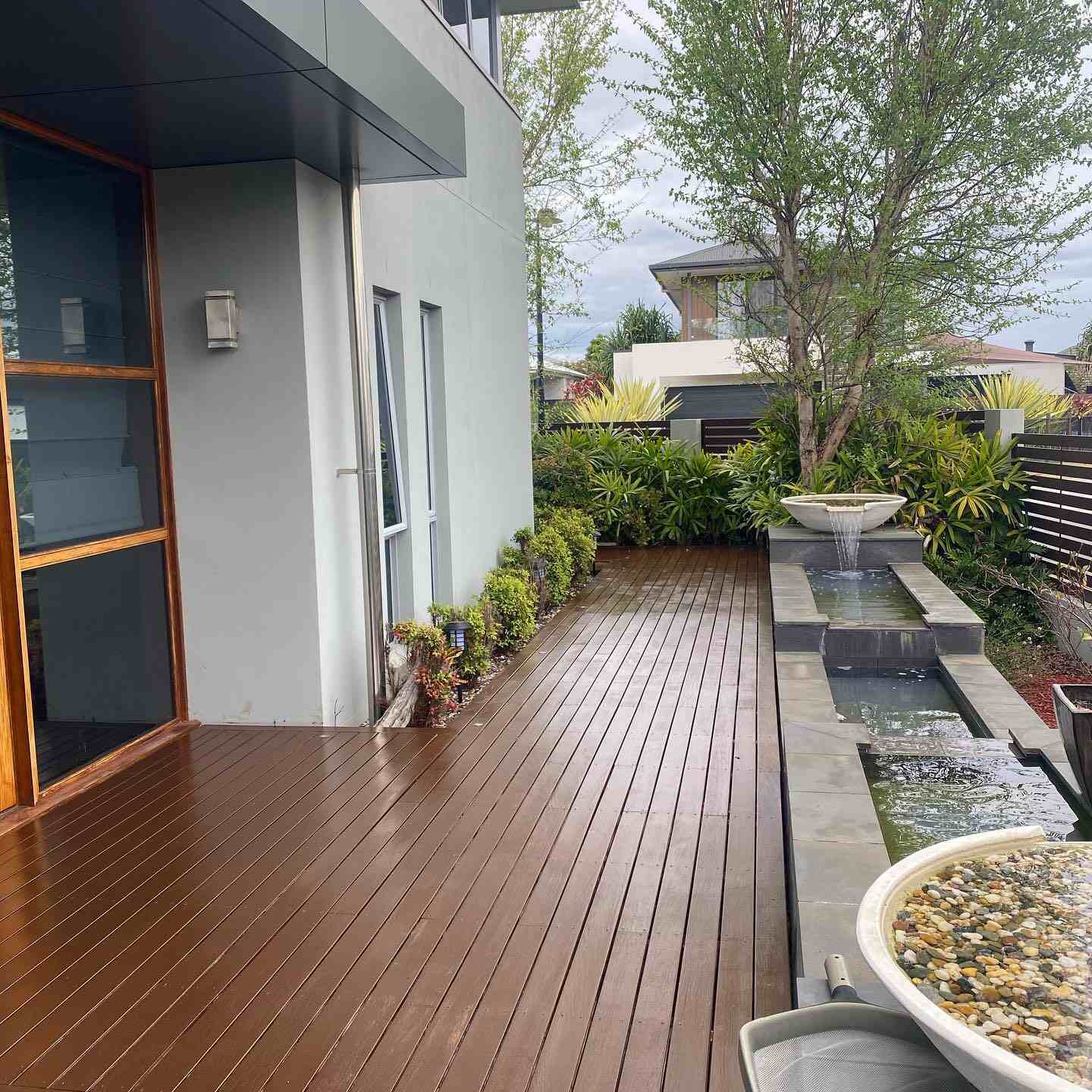Oiled timber side deck beside a water feature and rendered house